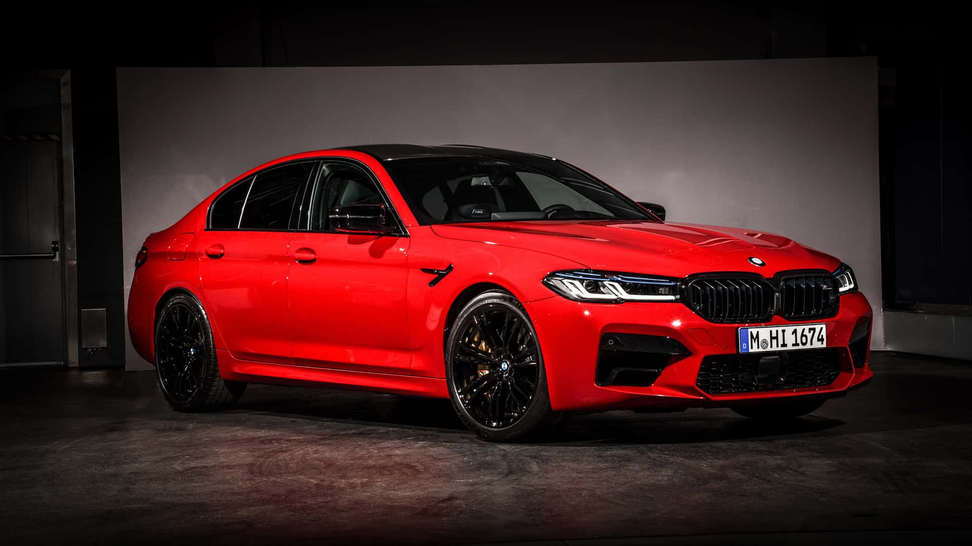 在黑暗的工作室環境中，紅色BMW M5轎車配備黑色輪圈。