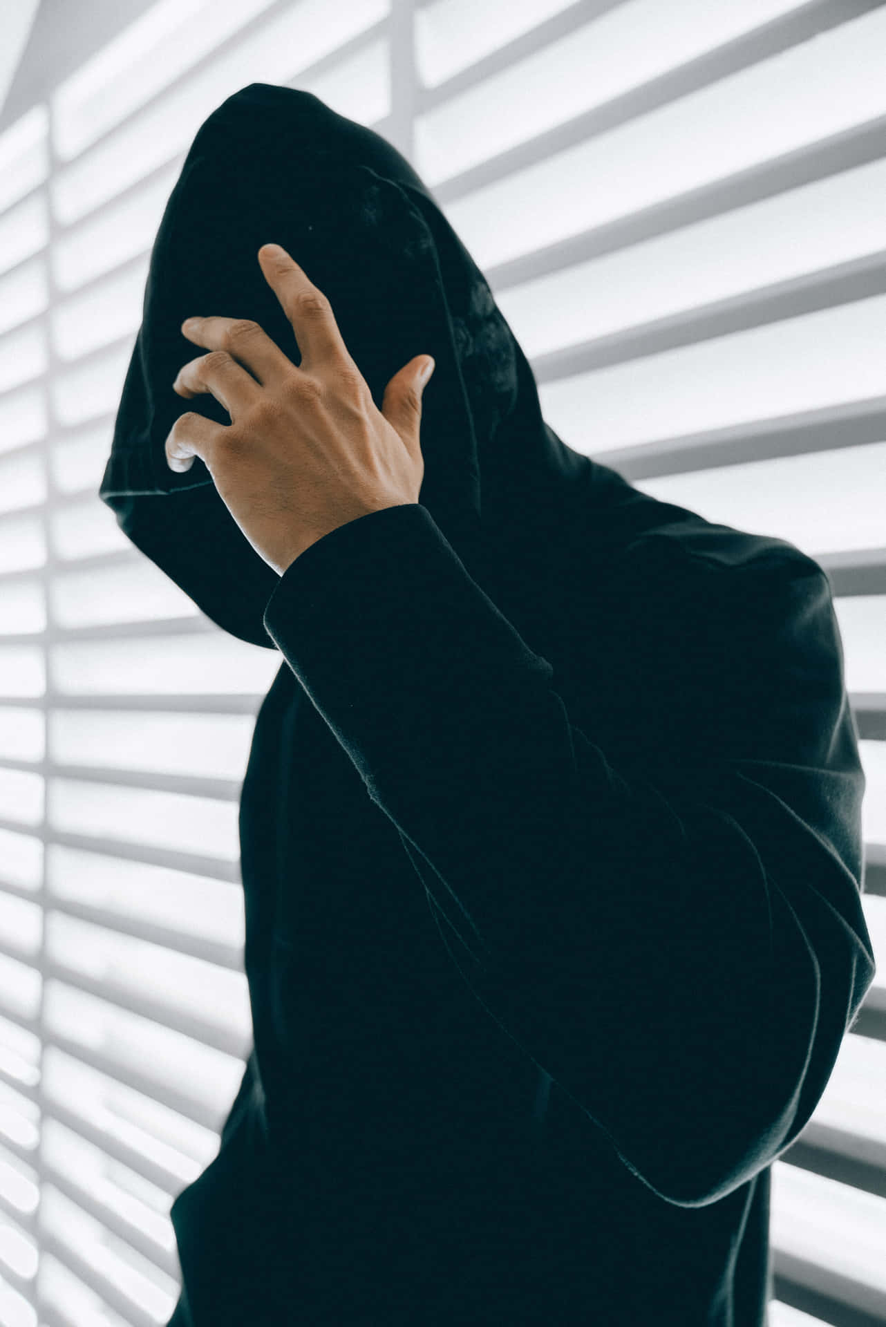 穿著黑色連帽衫的人在窗簾附近將帽子拉過臉部