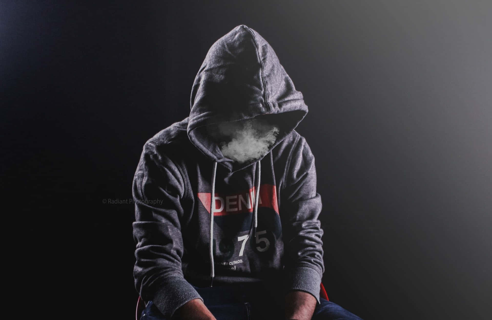 穿著深色連帽衫的人在昏暗光線下呼出煙霧。