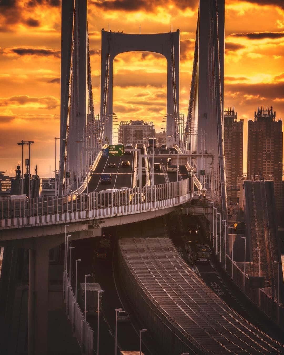 連接日本odaiba與shimauma的壯麗彩虹橋 壁紙 — 戲劇性的夕陽將東京的彩虹橋沐浴在金色光芒中，車輛在繁忙的城市高速公路上的橋樑跨度上流動。