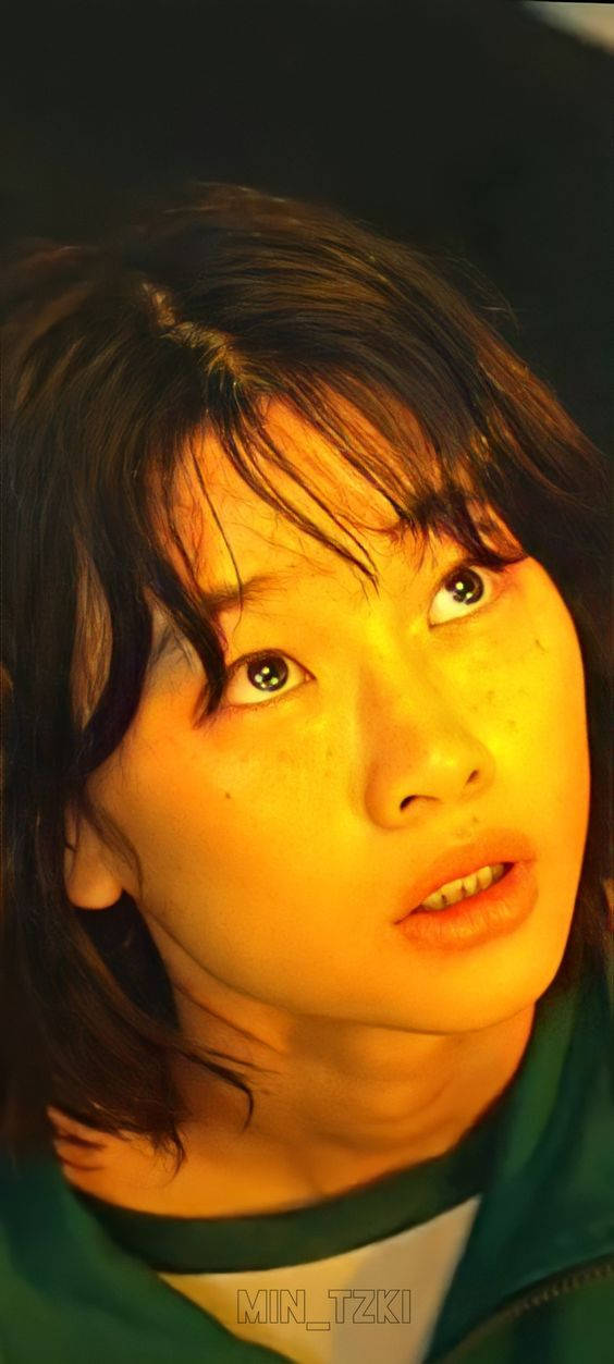 連結首爾兩岸的橋樑 壁紙 — 一個年輕黑髮雀斑女性的特寫肖像，沐浴在溫暖的金色光線中，背景為深色。