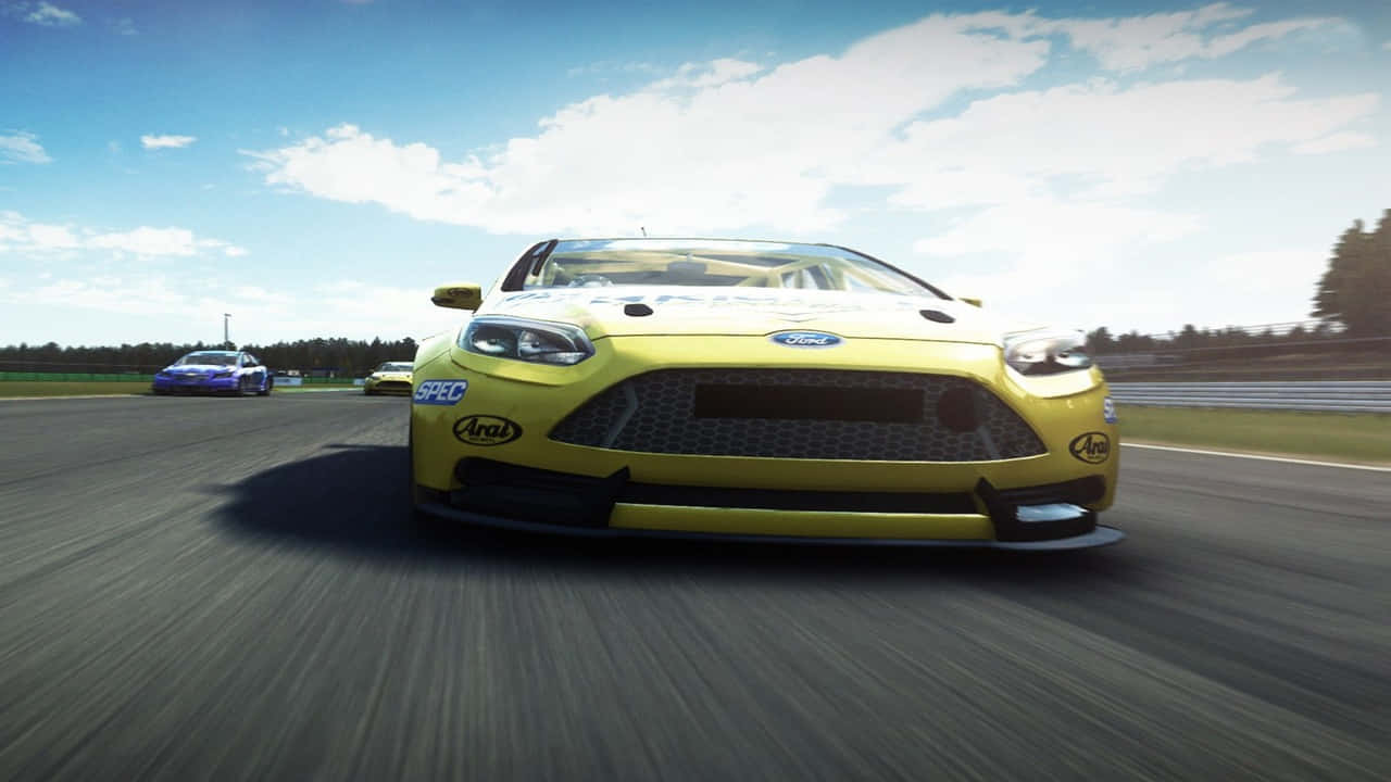 進入《Grid Autosport》的高燃競技賽車世界 壁紙 — 一架鮮黃色的福特賽車在陽光明媚的賽道上疾馳，背景模糊，頭頂藍天。