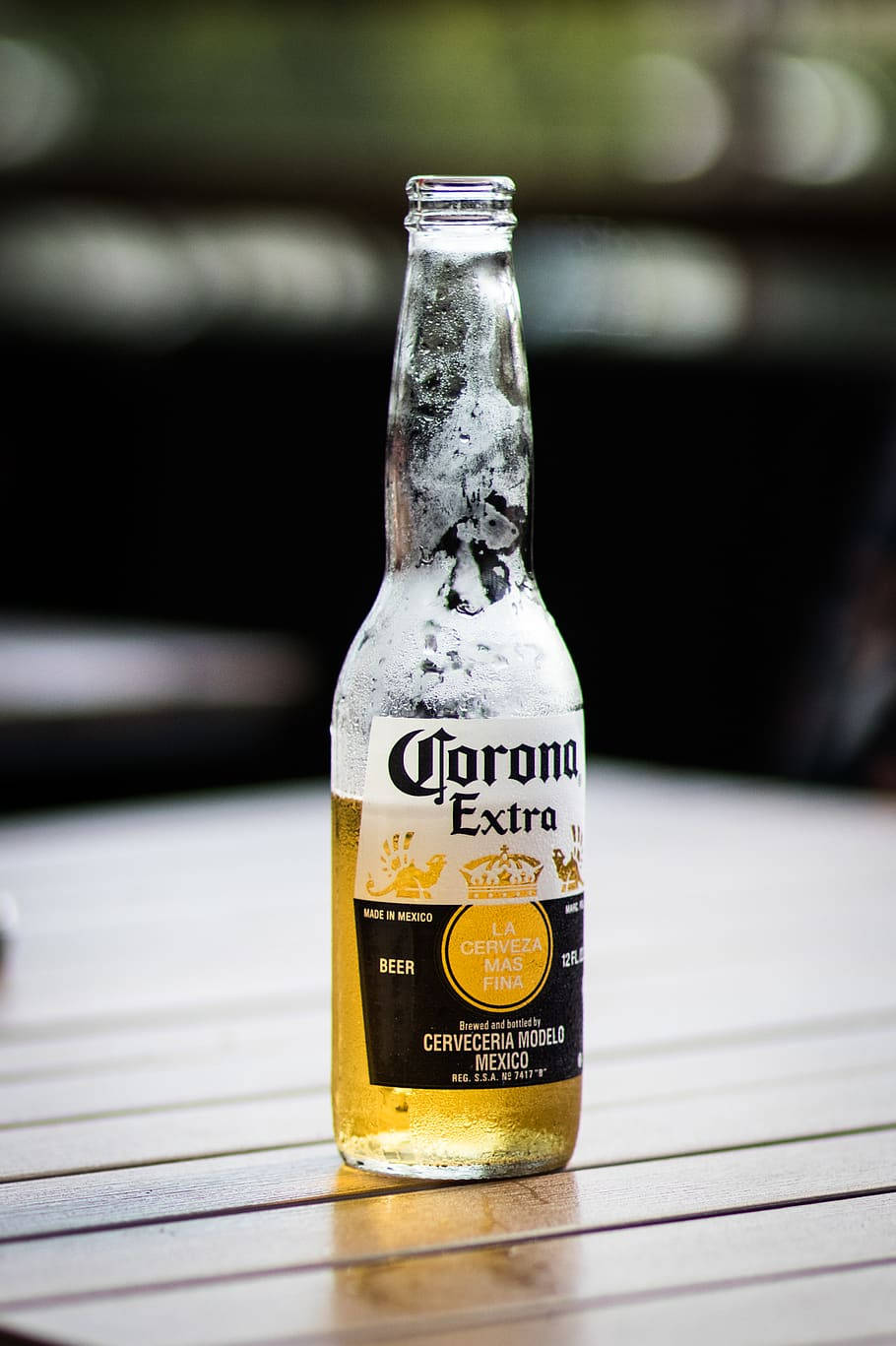 進口墨西哥Corona Extra啤酒 壁紙 — 一瓶冰凍的Corona Extra啤酒，帶有水珠，放在戶外的木桌上。