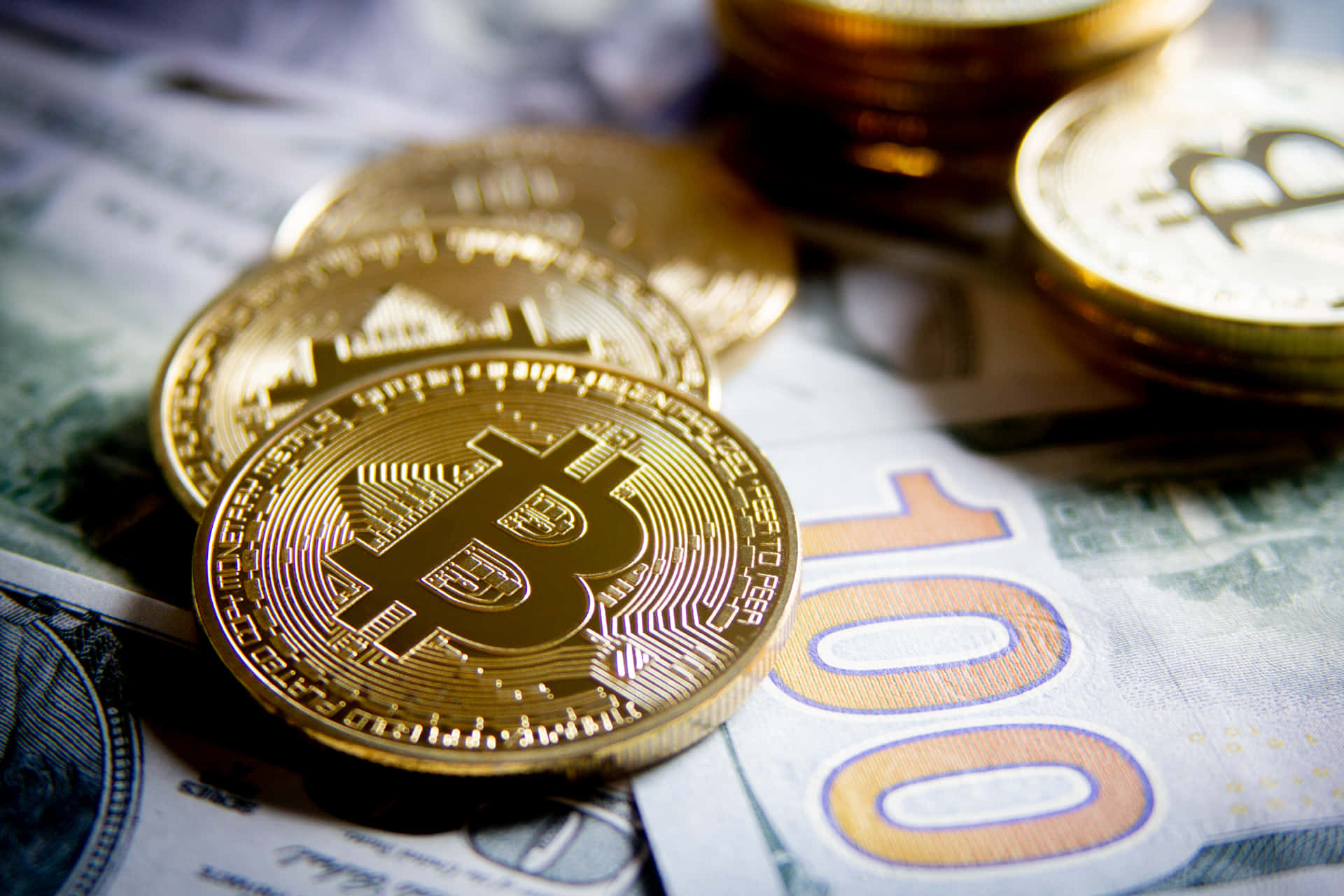 進行數位投資：探索比特幣的潛力 壁紙 — 金色比特幣硬幣放在一百美元鈔票和歐元鈔票上，特寫金融構圖。
