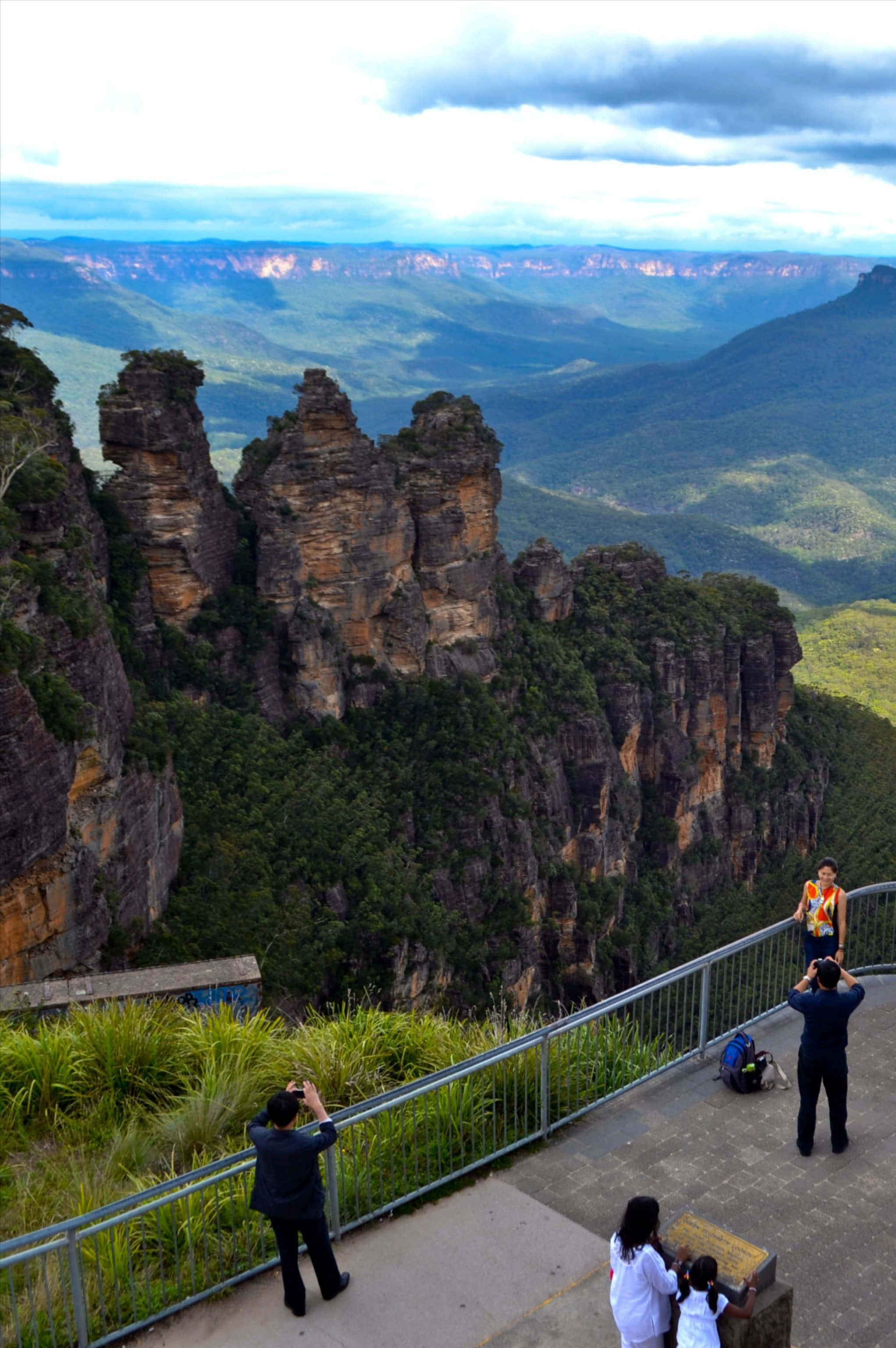 Blue Mountains National Park 桌布 壁紙 — 遊客在標誌性的三姊妹岩層前拍照，俯瞰雲天下廣闊的綠色山谷。