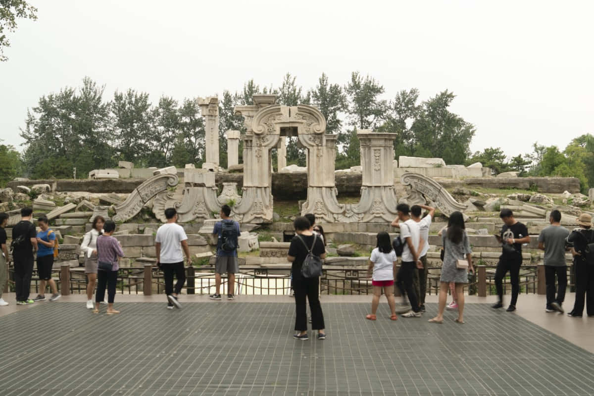 遊客聚集於圓明園 壁紙 — 遊客在陰天探索宏偉宮殿花園中風化的石頭廢墟。