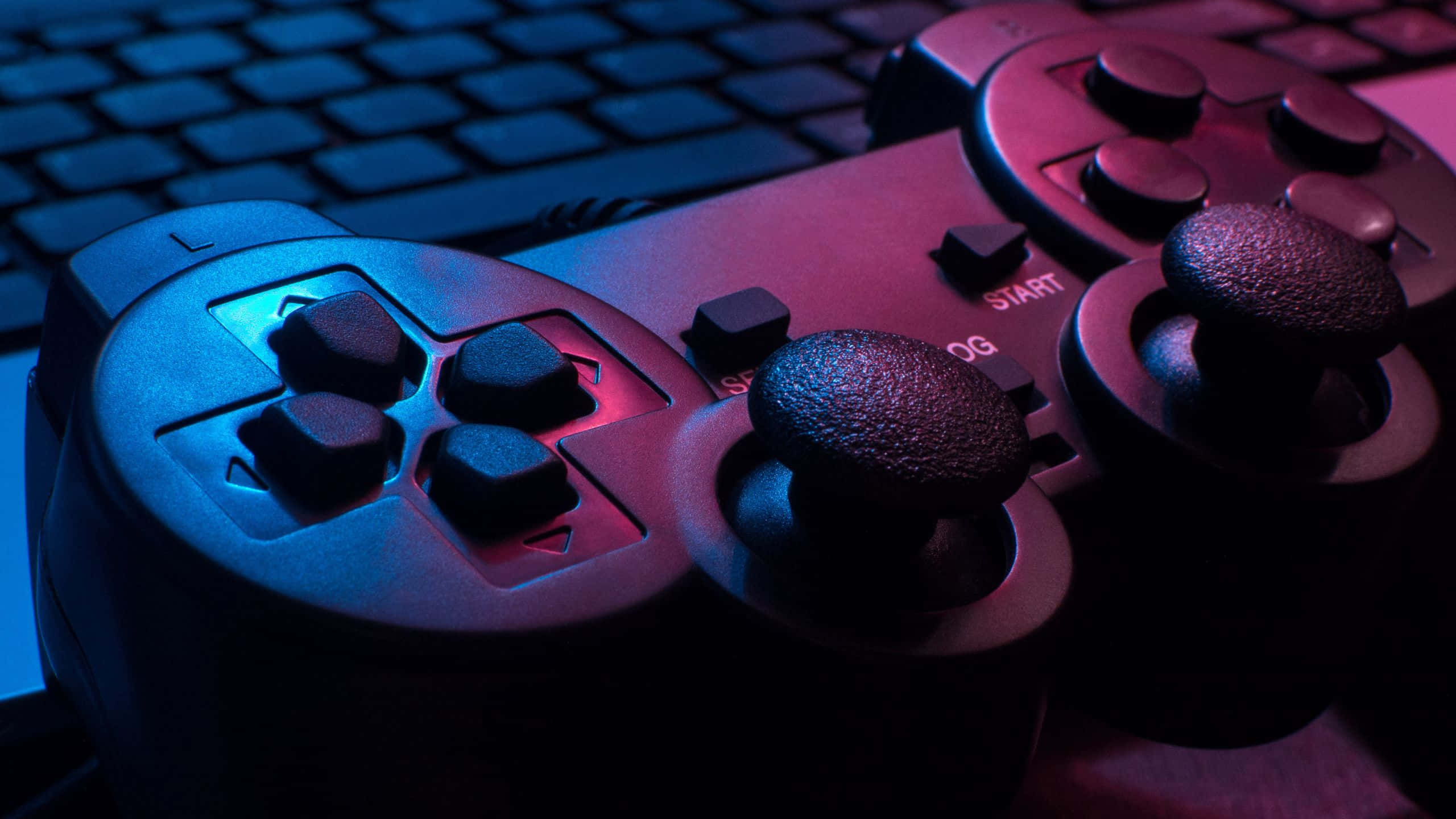 Gaming Banner 桌布 壁紙 — 遊戲控制器嘅特寫，沐浴喺藍色同粉紅色霓虹燈光下，放喺鍵盤上面。