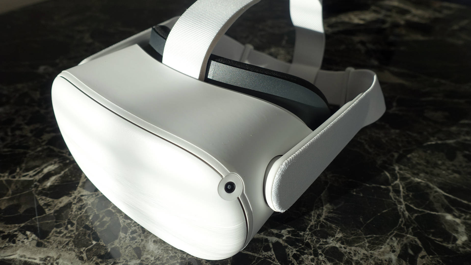 遊戲用Oculus Quest 2裝置 壁紙 — 一個時尚的白色VR頭戴式裝置放在深色帶紋理的大理石表面上，光線柔和。