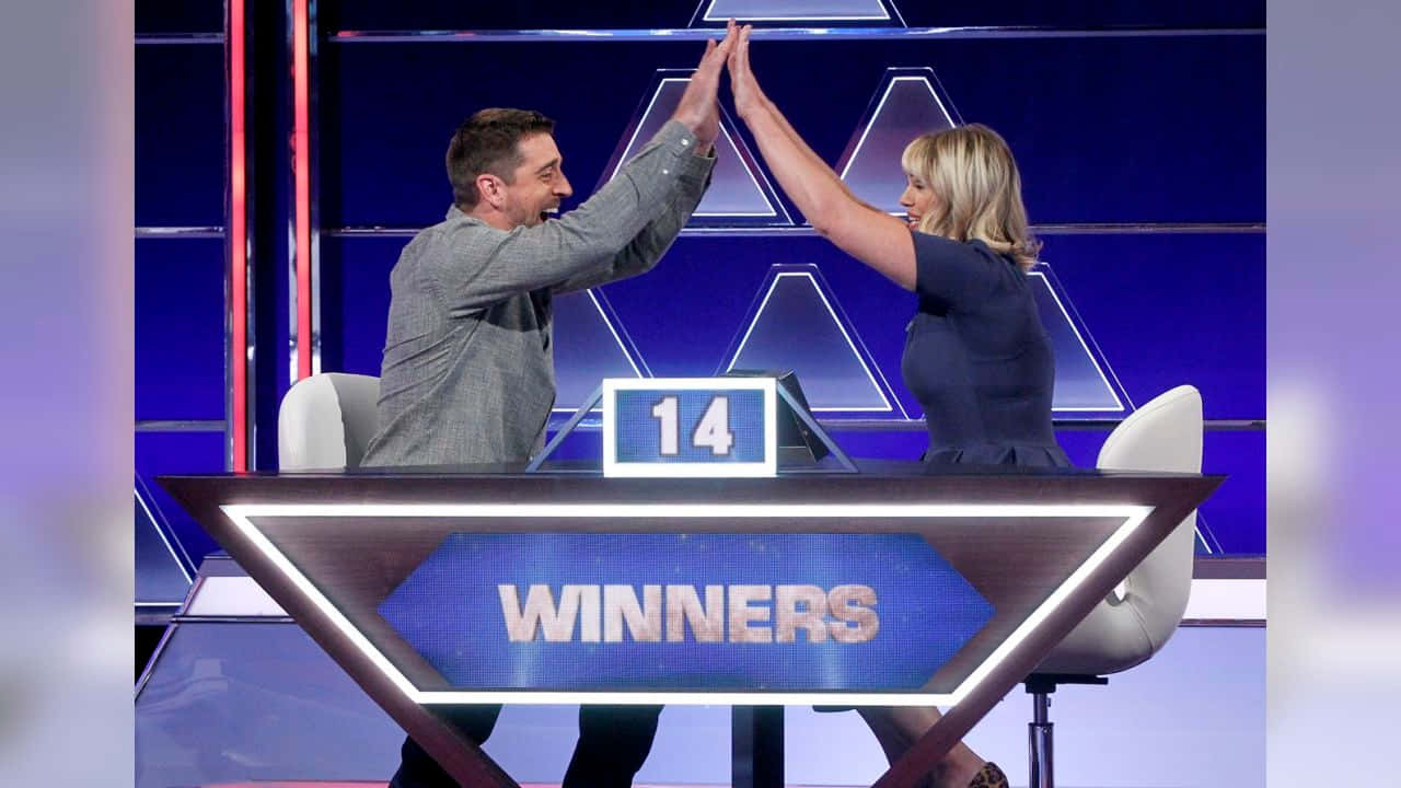 遊戲節目冠軍擊掌高五照片 壁紙 — 兩位遊戲節目參賽者在發光的「WINNERS」頒獎台上擊掌，顯示參賽者號碼14。