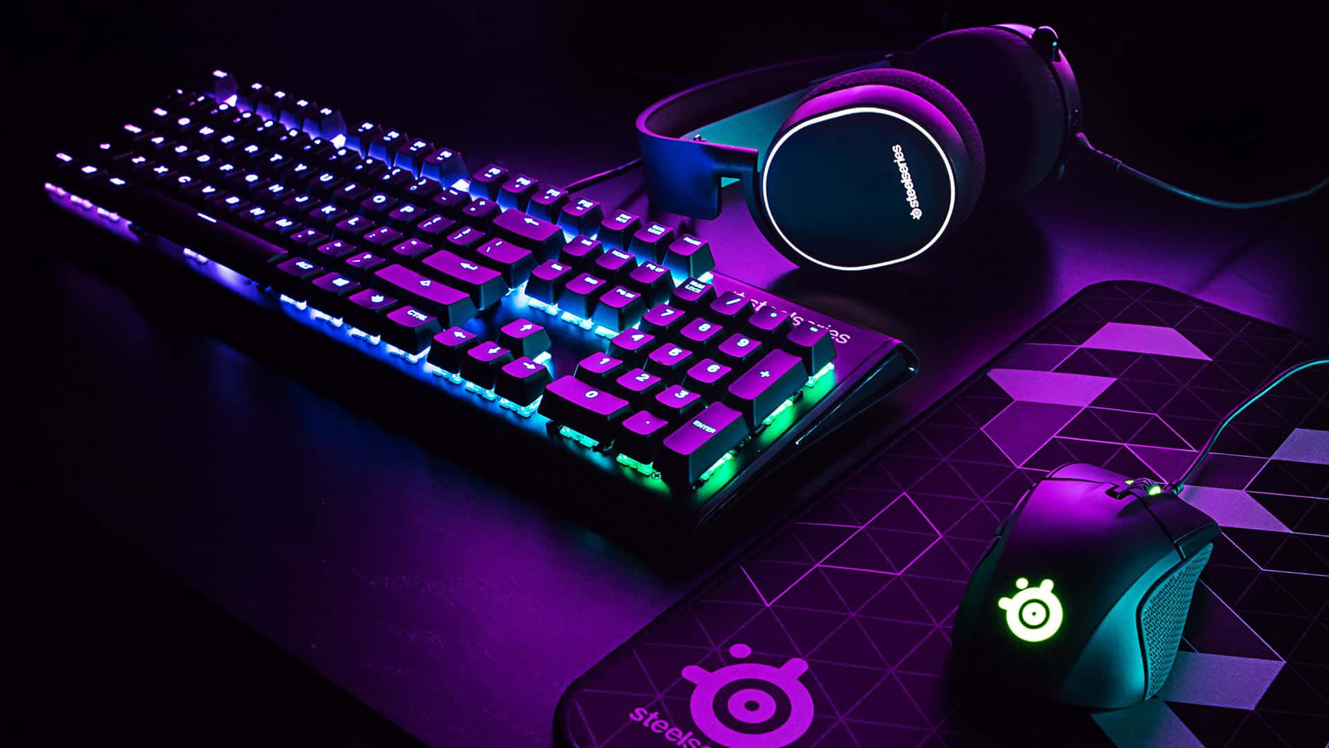 Gaming Mouse 桌布 壁紙 — 遊戲設置，配備發光鍵盤、滑鼠和耳機，在黑暗的桌子上沐浴在紫色和藍色的霓虹燈光中。