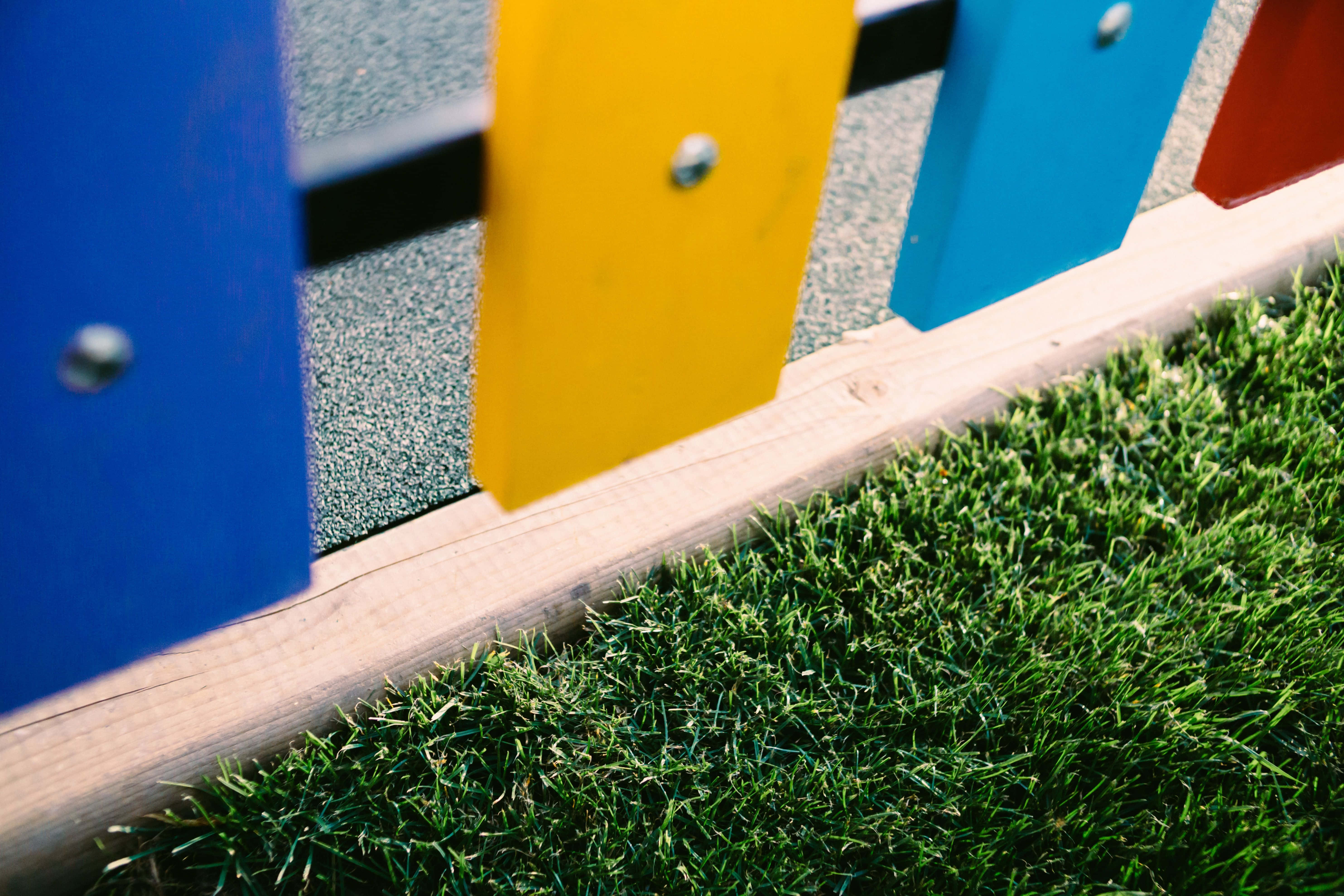Playground 桌布 壁紙 — 遊樂場圍欄上充滿活力的藍色、黃色和紅色面板，矗立在茂盛的綠色草地上，沐浴在明亮的陽光下。