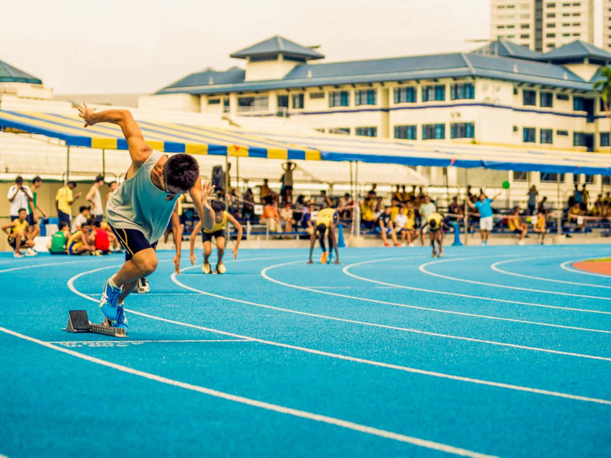 sport 桌布 壁紙 — 運動員在充滿活力的藍色跑道上衝刺，背景有觀眾和建築物。