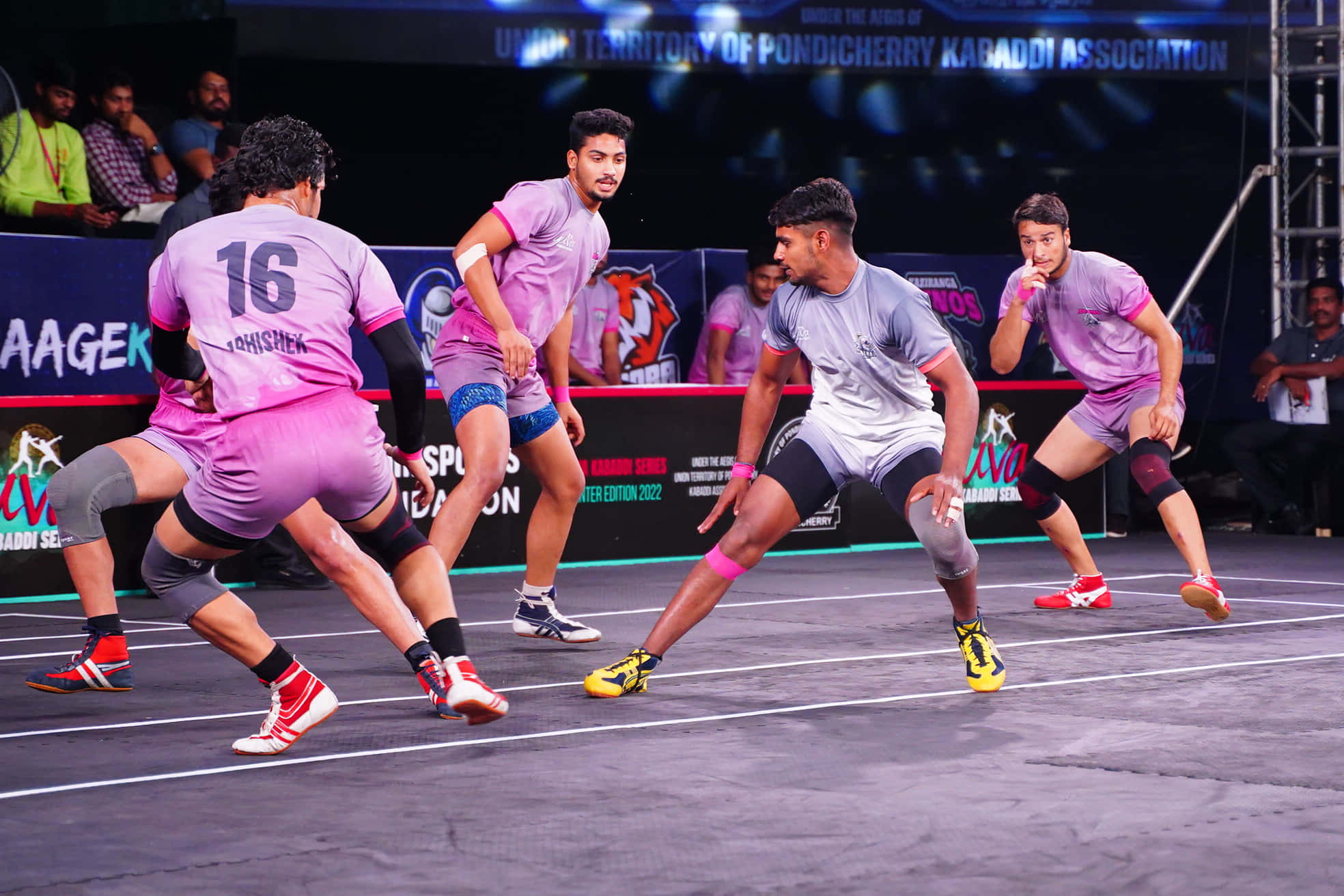 Kabaddi 桌布 壁紙 — 運動員穿著粉紅色和灰色制服，在明亮的場館燈光下激烈地進行卡巴迪比賽。