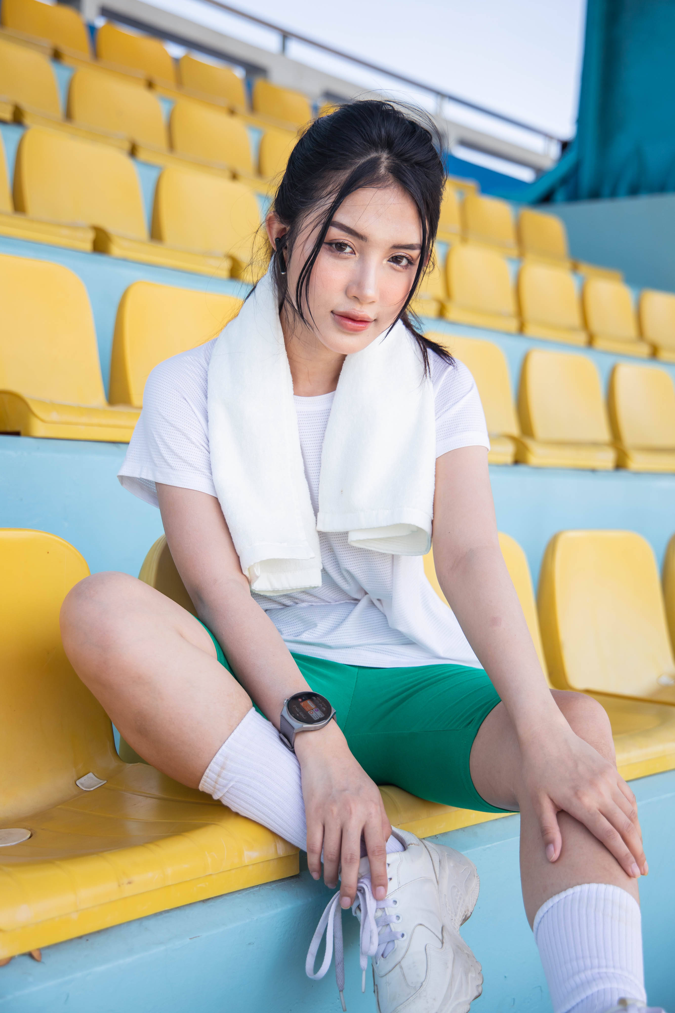 運動女性佩戴智能手錶 壁紙 — 一位身穿運動服的年輕女性坐在亮黃色的體育場座位上，肩上披著毛巾。