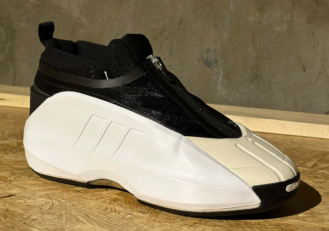 運動時尚與性能的完美結合 — Adidas 壁紙 — 一對未來感黑白運動鞋，帶拉鏈，放在木質表面上，背景是混凝土牆。