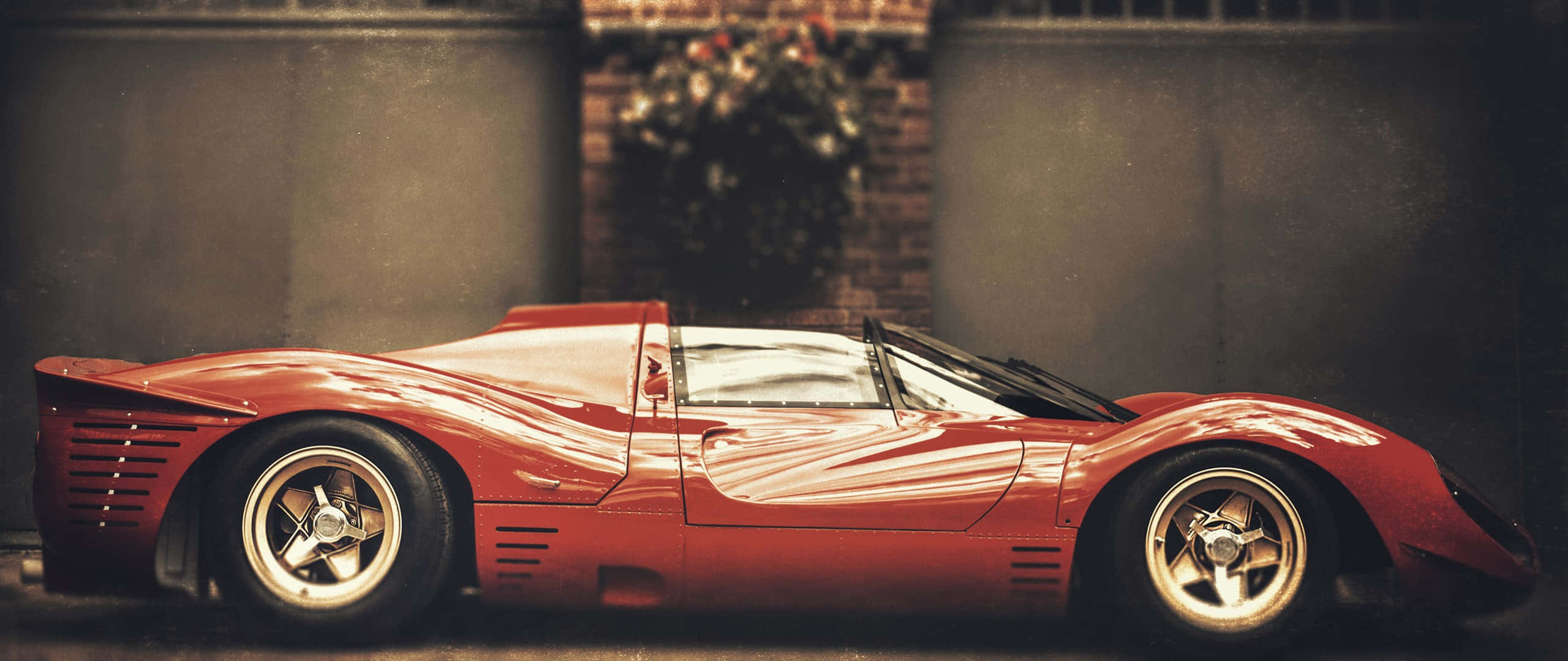 運動跑車卓越的經典之美 壁紙 — 一輛帶有白色條紋的時尚紅色復古賽車，在溫暖的燈光下，以磚牆為背景閃閃發光。