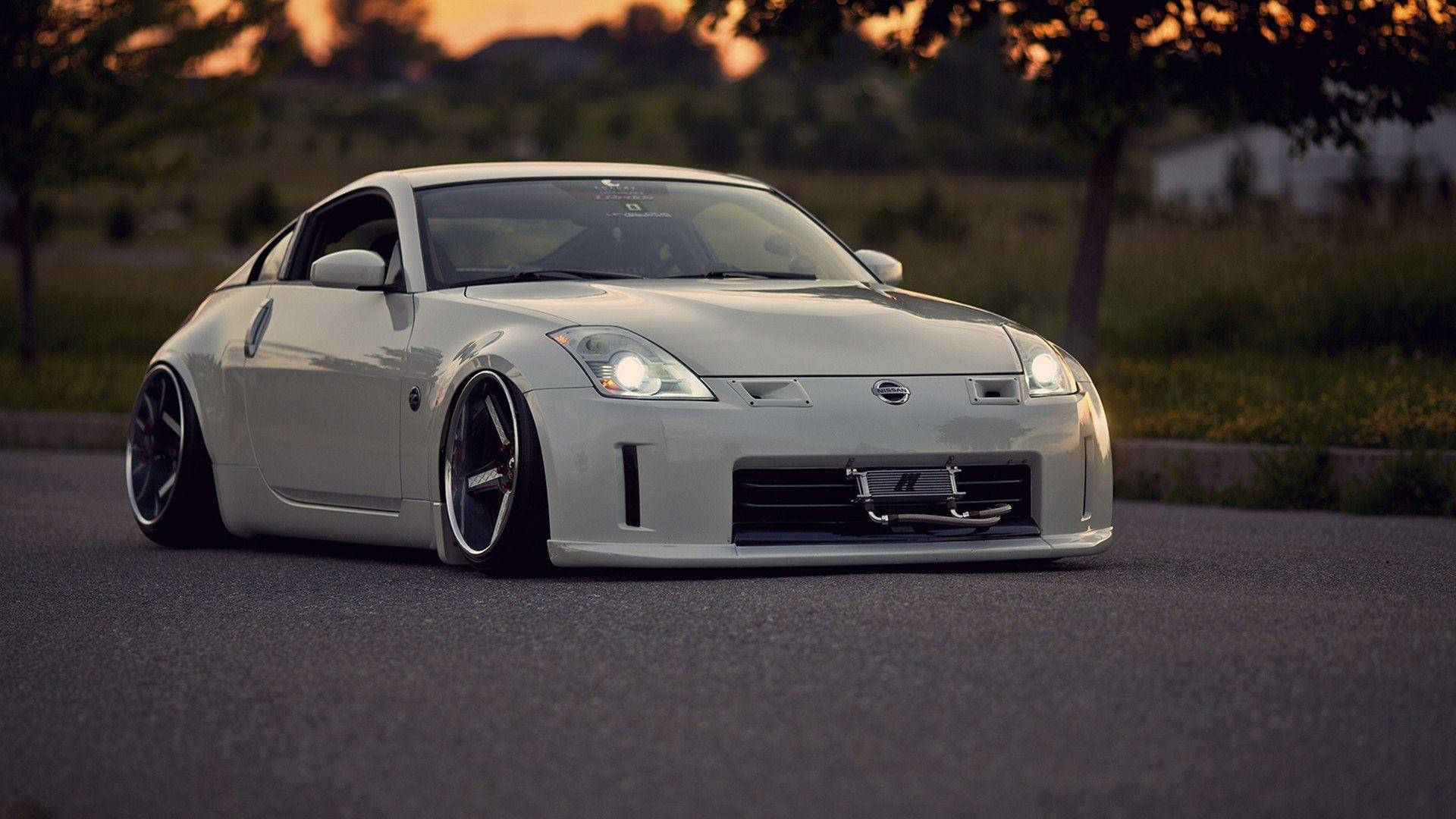 運動車巔峰之作：Nissan 350Z 壁紙 — 一架線條流暢的白色日產350Z跑車，配備降低懸掛和發光頭燈，在日落時分停泊在瀝青路上。