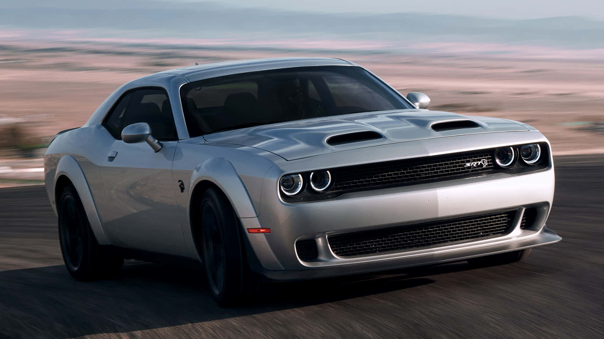 銀色 Dodge Challenger SRT 在黃昏時分的沙漠公路上飛馳。