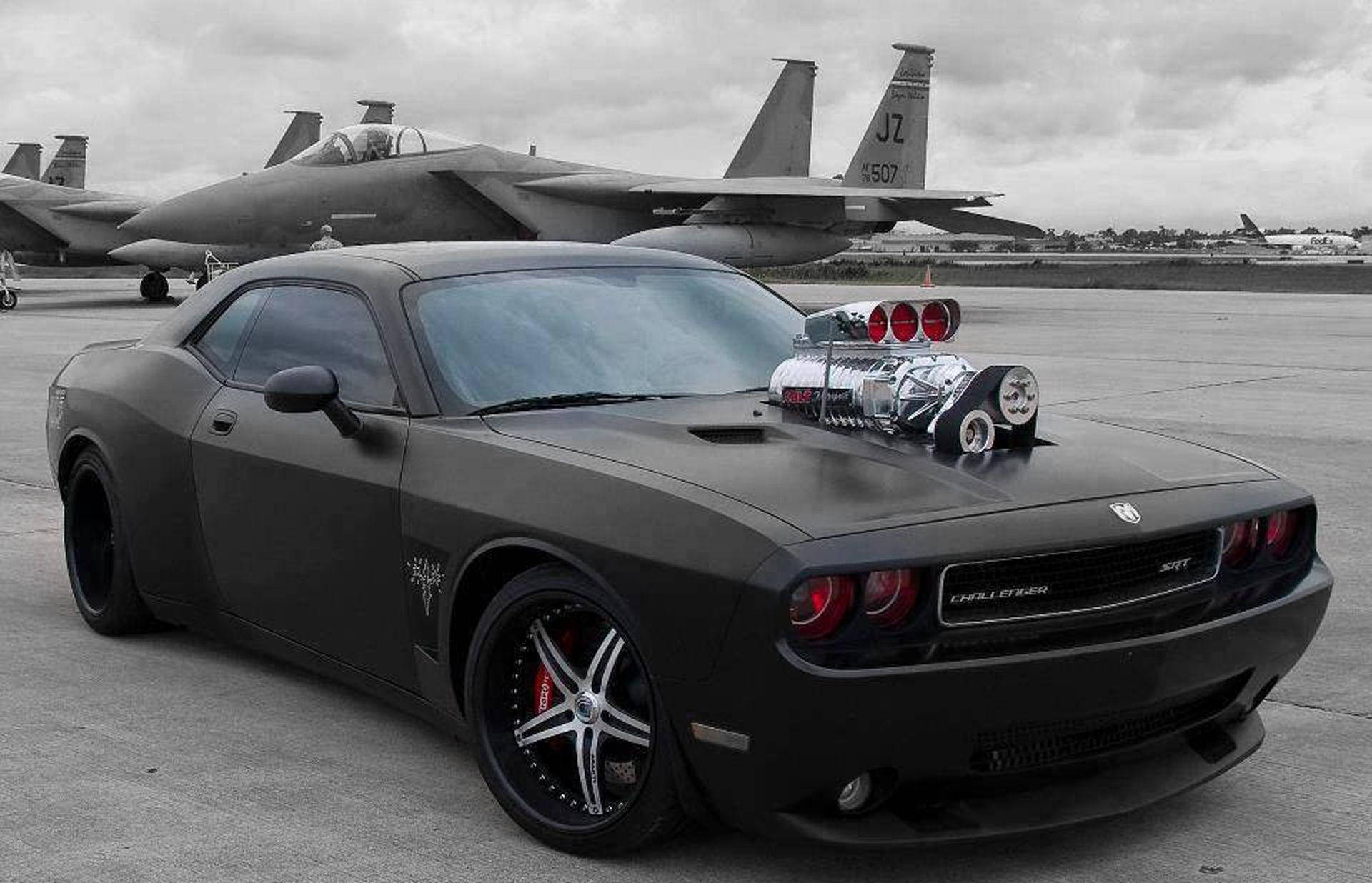 黑色肌肉車配增壓器停在停機坪上，靠近戰鬥機。 — Dodge challenger GIF 壁紙