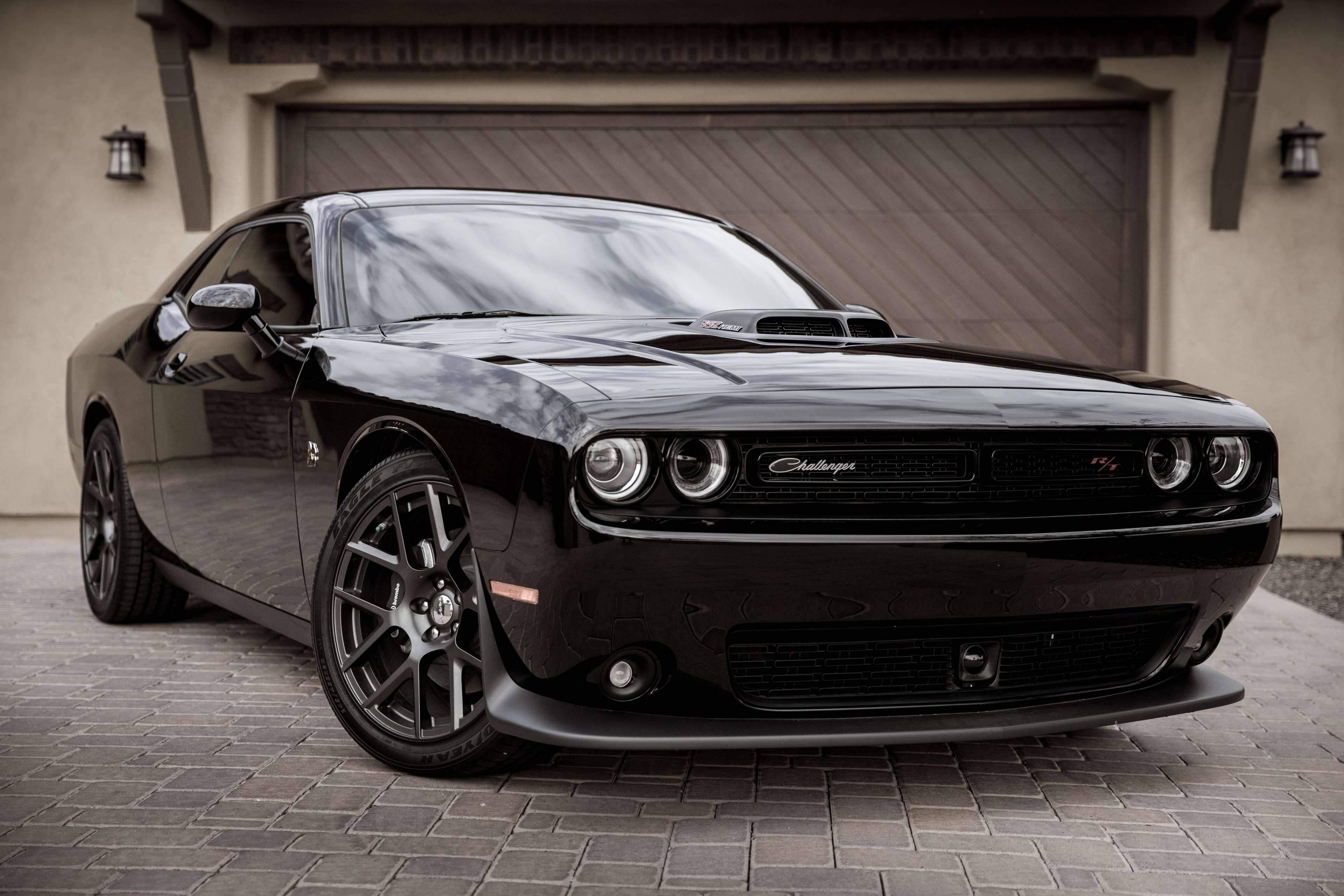 道奇挑戰者Hemi 壁紙 — 一輛亮黑色Dodge Challenger SRT停泊在車庫前的石頭車道上，車庫有溫暖的環境照明。