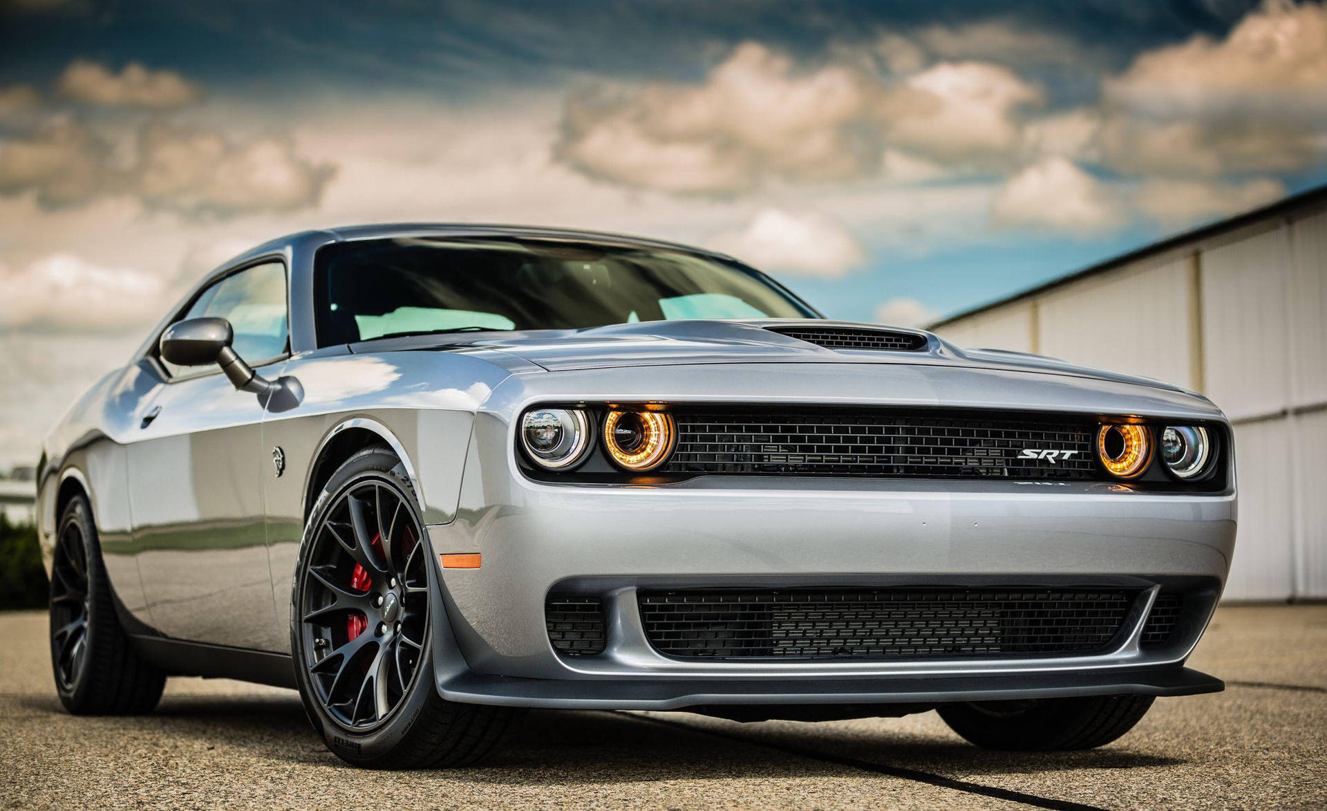 銀色Dodge Challenger SRT，帶有橙色頭燈，停在陰天天空下的戶外。 — Dodge challenger GIF 壁紙