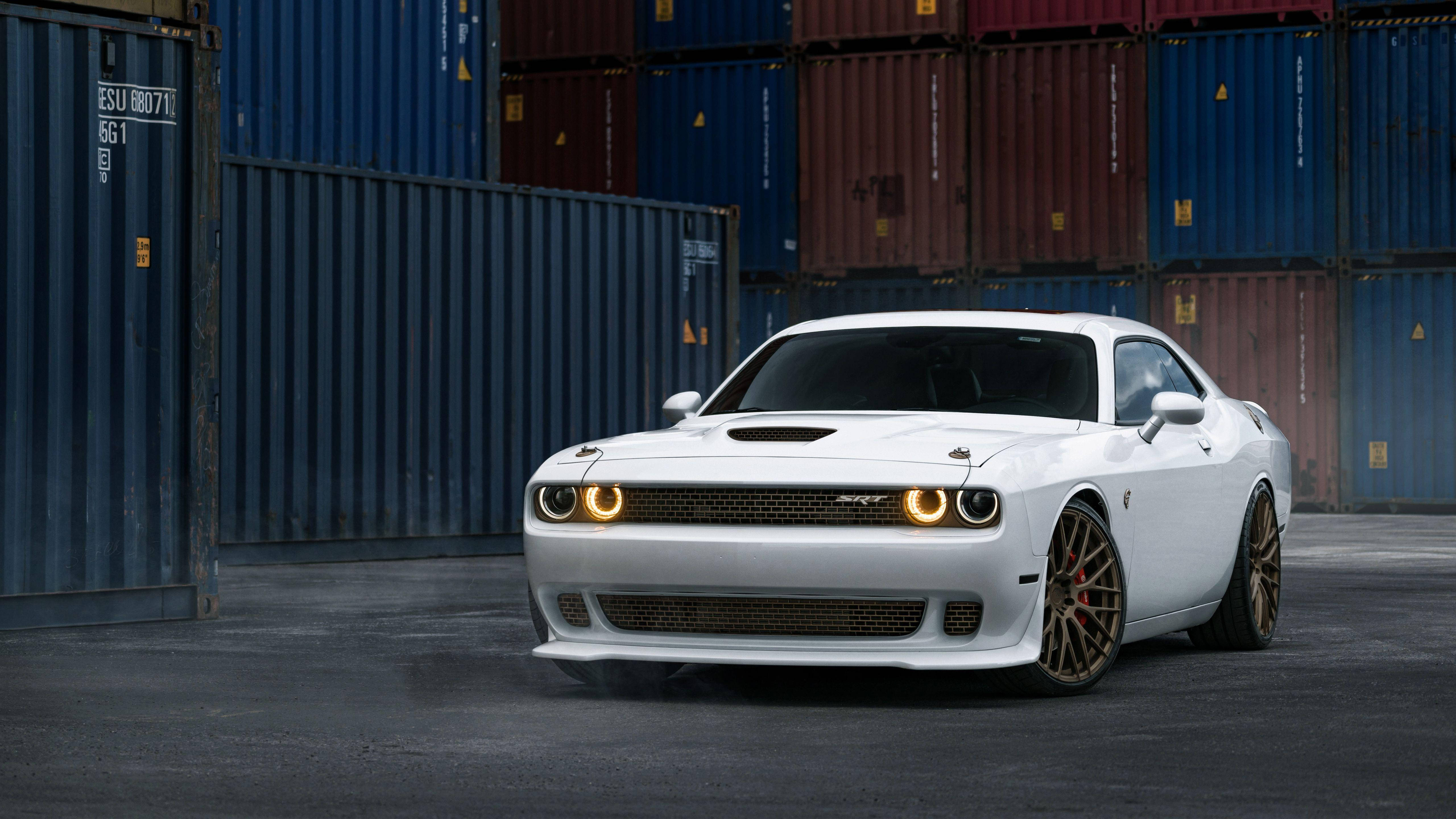 道奇挑戰者自訂白色指節塗裝 壁紙 — 一輛白色 Dodge Challenger SRT Hellcat 亮著車頭燈，停在堆疊的藍色和紅色貨櫃前。