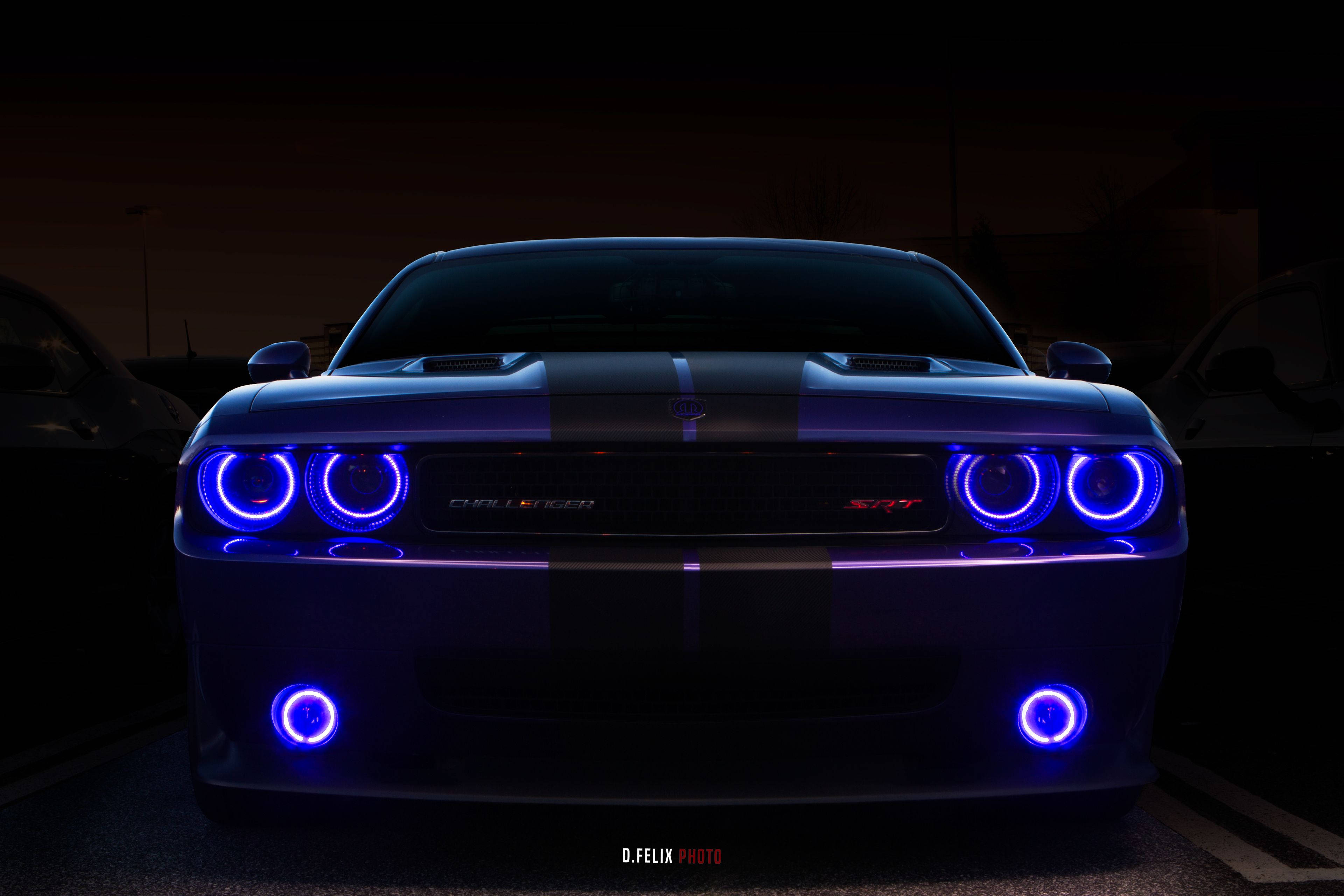 道奇挑戰者配備天使燈 壁紙 — 一輛黑色Dodge Challenger SRT，帶有發光的藍色圓形頭燈和底盤燈，在黑暗的停車場中威嚴地矗立。
