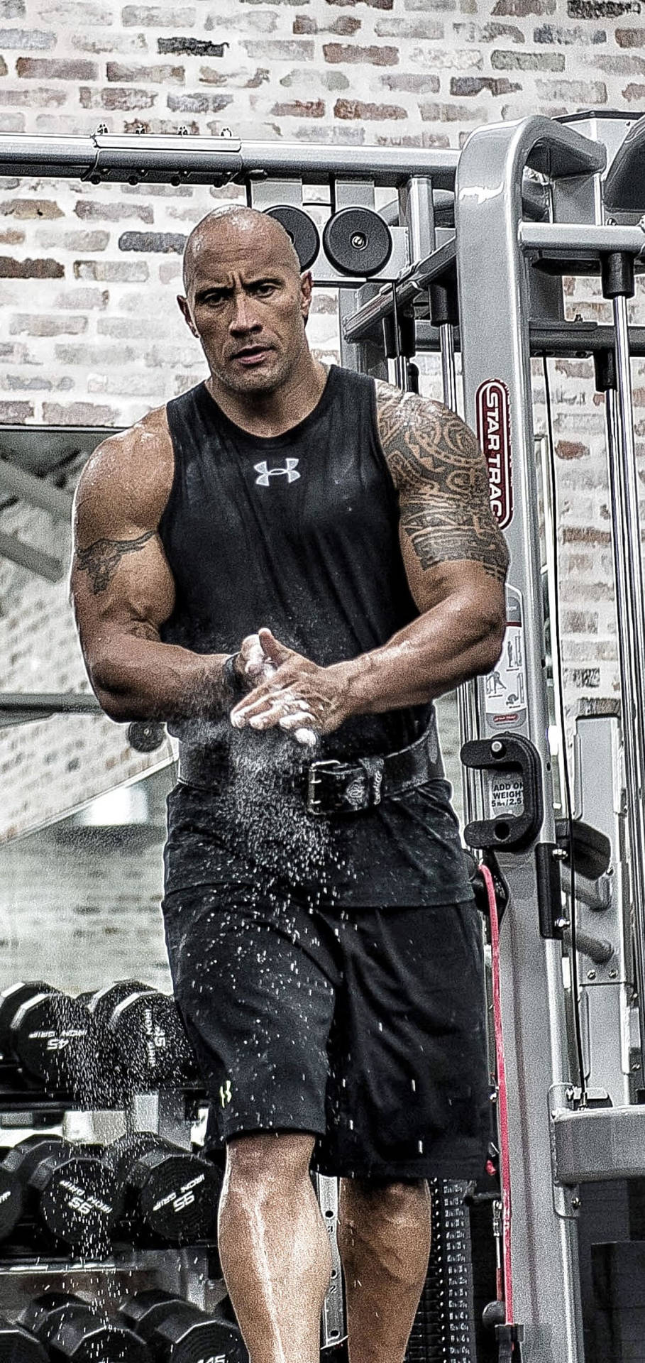 Dwayne Johnson 在磚牆健身室中拍打粉筆灰。