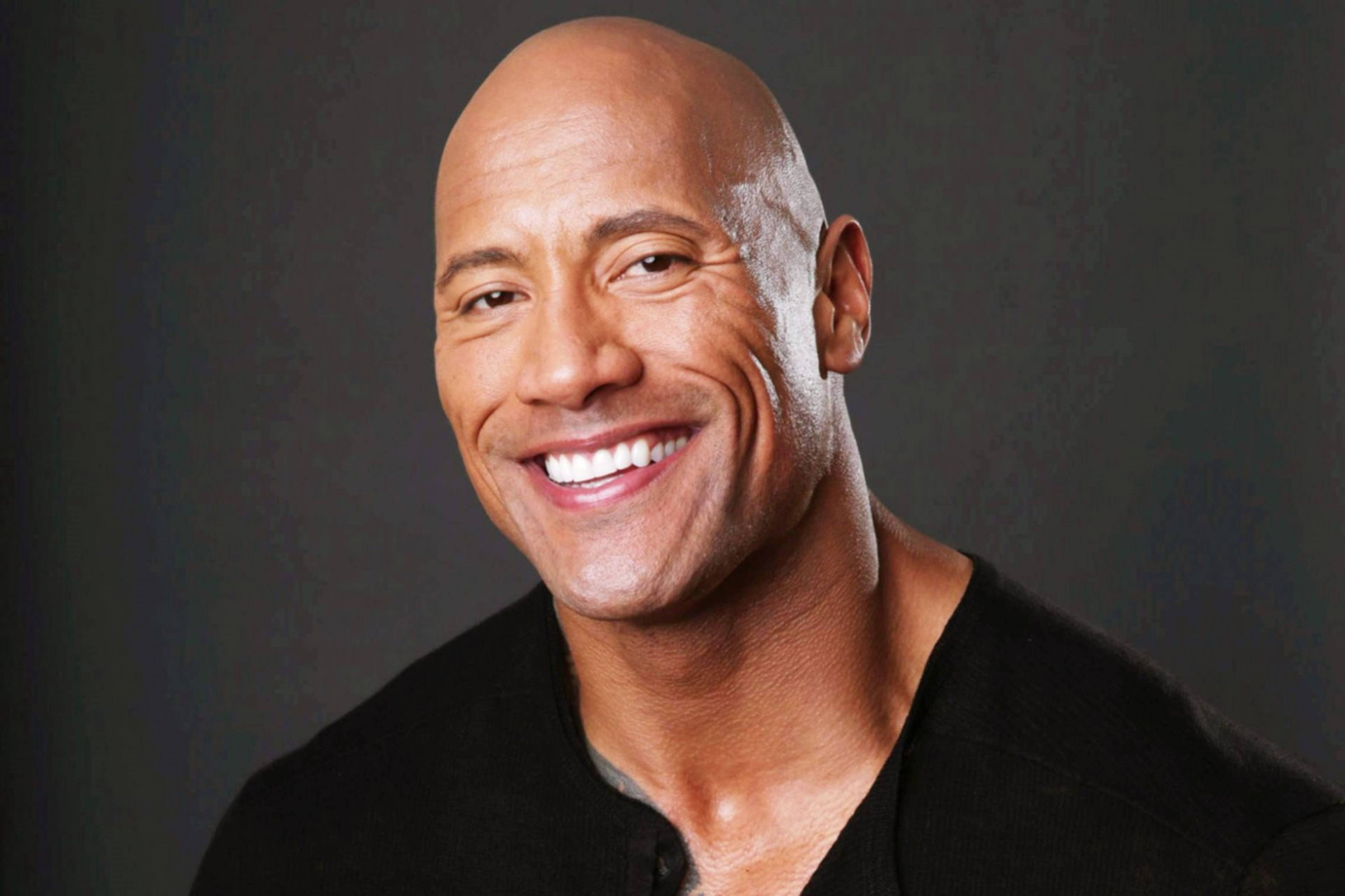 道恩·強森展露燦爛笑容 壁紙 — Dwayne Johnson 喺深灰色工作室背景前燦爛微笑嘅特寫肖像。