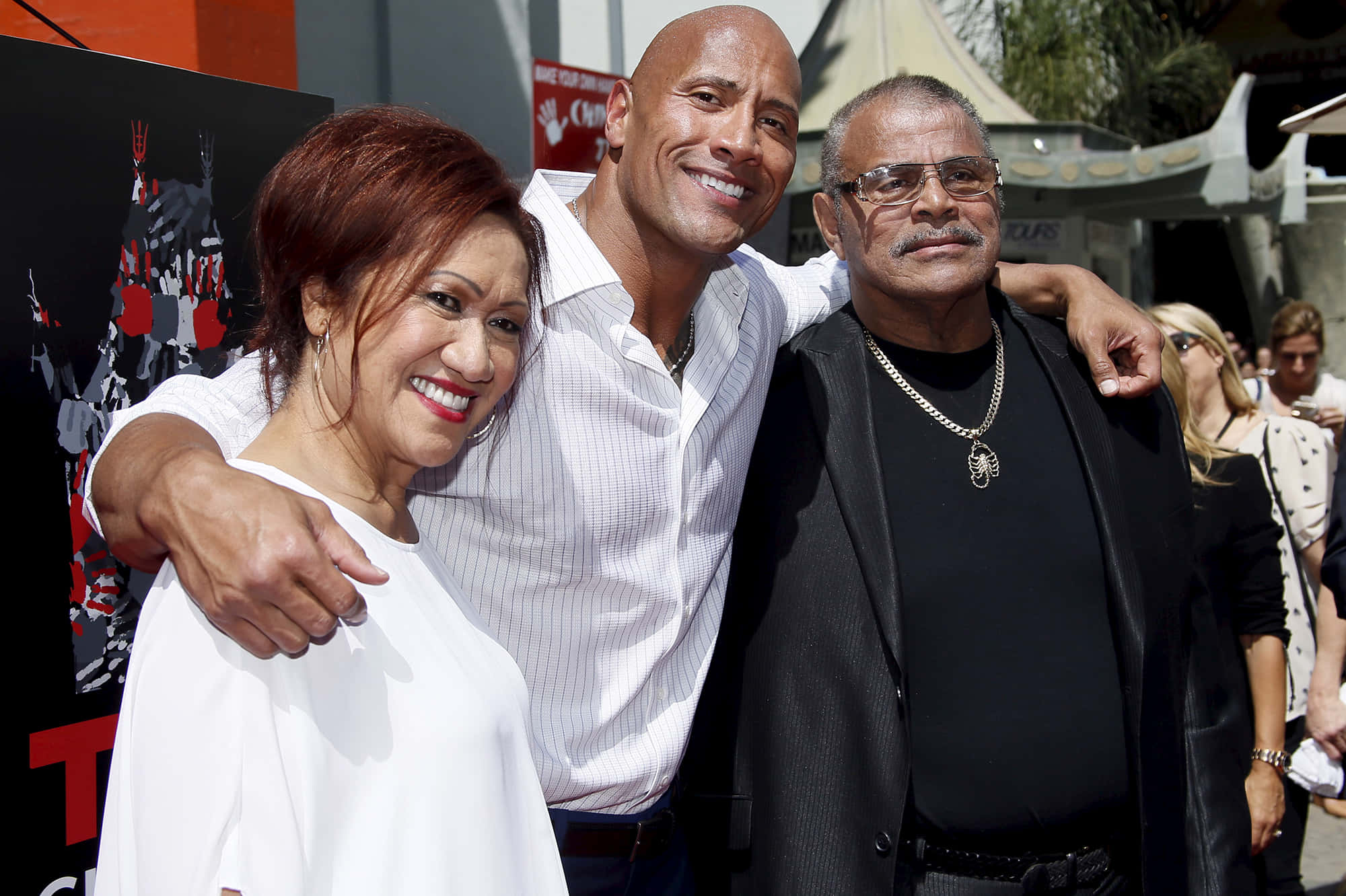 道恩·強森與父母阿塔及洛克·強森於2015年5月 壁紙 — Dwayne Johnson 在陽光明媚的戶外活動中與兩名男子一起露出燦爛笑容，姿勢隨意。