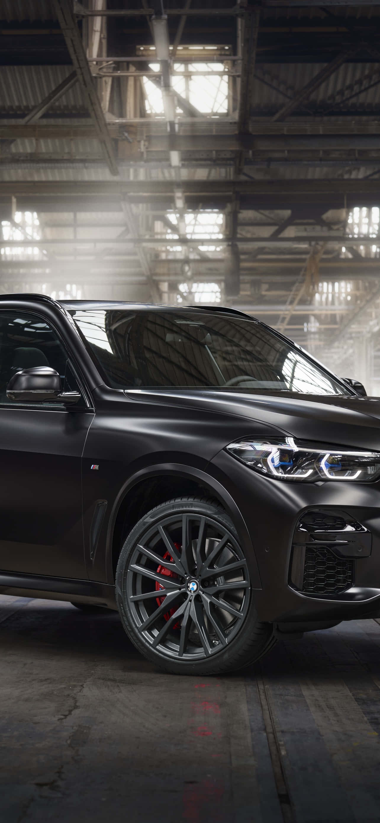 道路上令人印象深刻的BMW X6 M 壁紙 — 一輛啞光黑色BMW SUV，帶紅色制動卡鉗，停放在一個灰塵滿佈、高天花且陽光穿透的工業倉庫中。