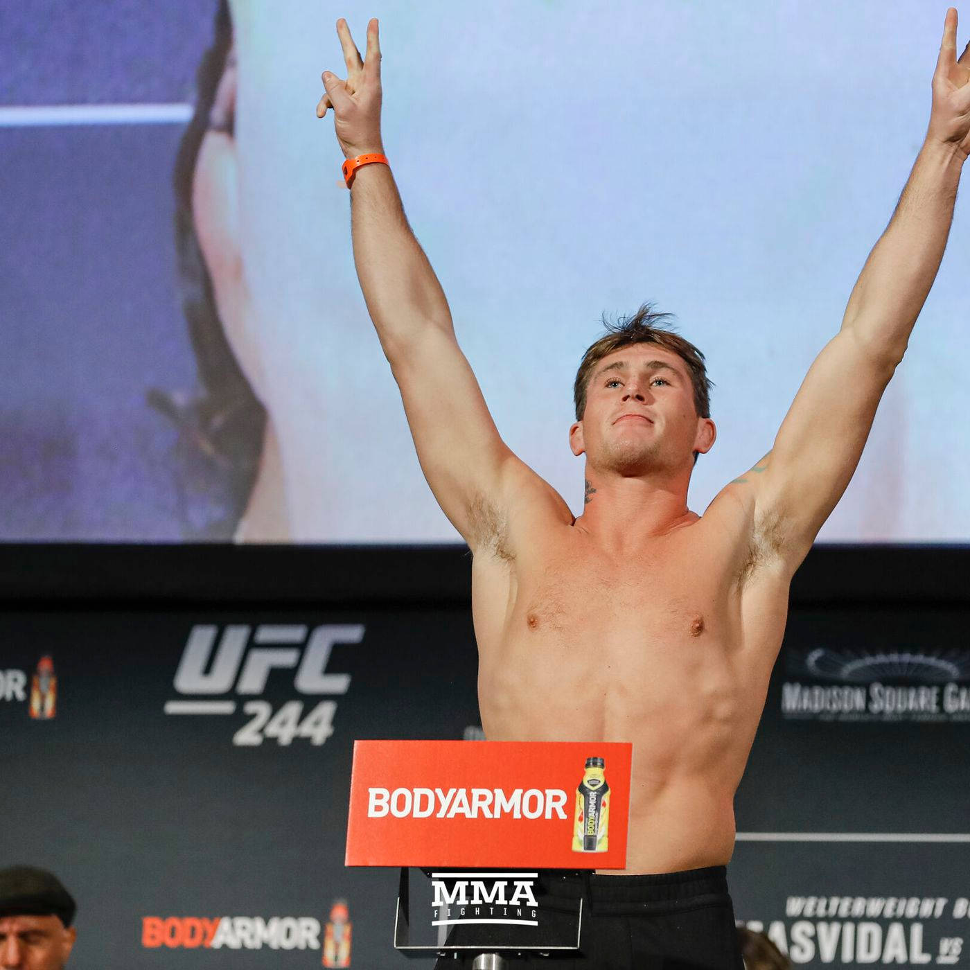 達倫·蒂爾於UFC 244 壁紙 — 一名赤裸上身的男拳手在UFC 244稱重活動中高舉雙臂慶祝勝利，身後有一個大屏幕。