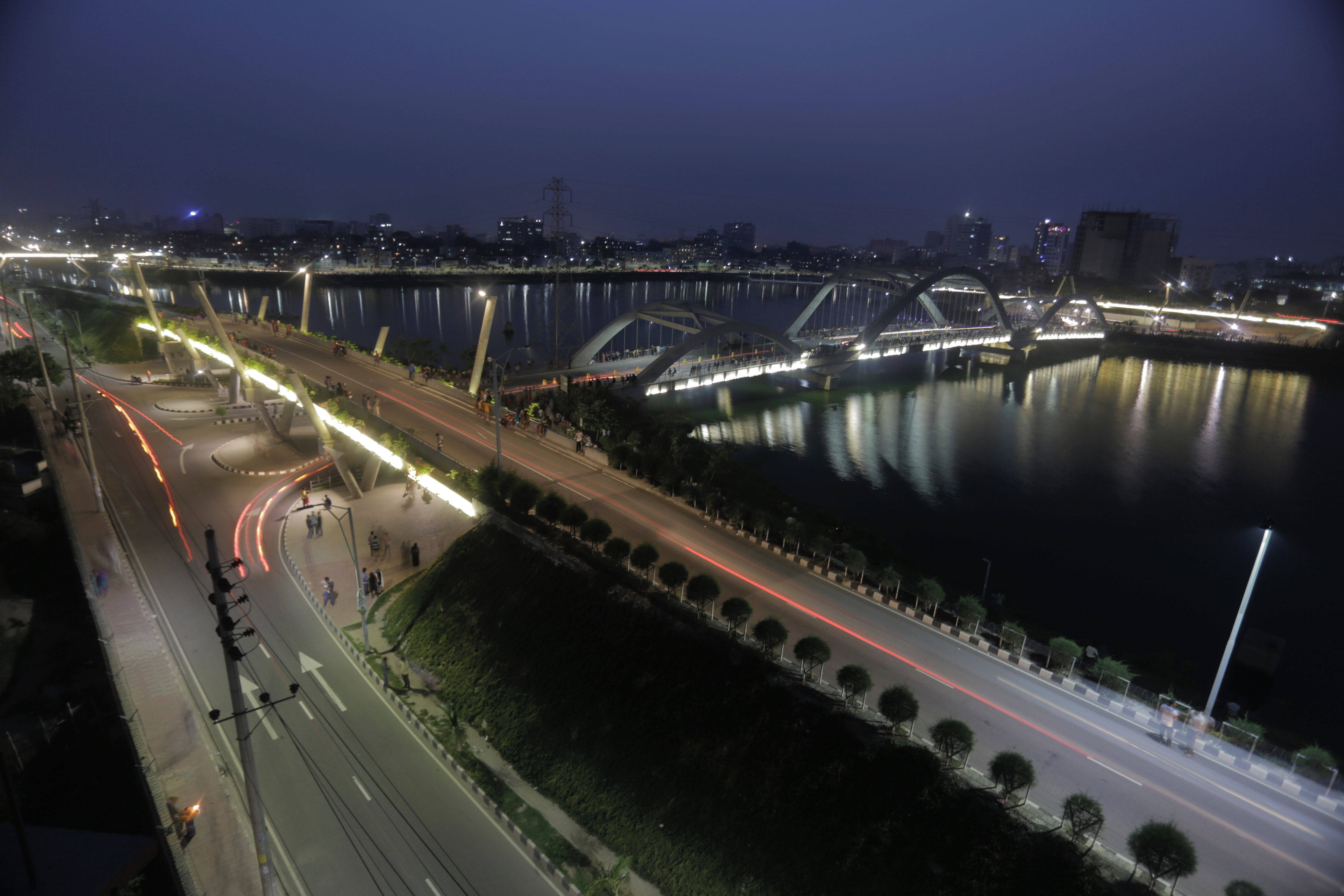 達卡哈提爾賈heel橋旁的長路 壁紙 — 充滿活力的夜景城市景觀，特色是燈光璀璨的橋樑和道路，在反射的河流上留下光跡。