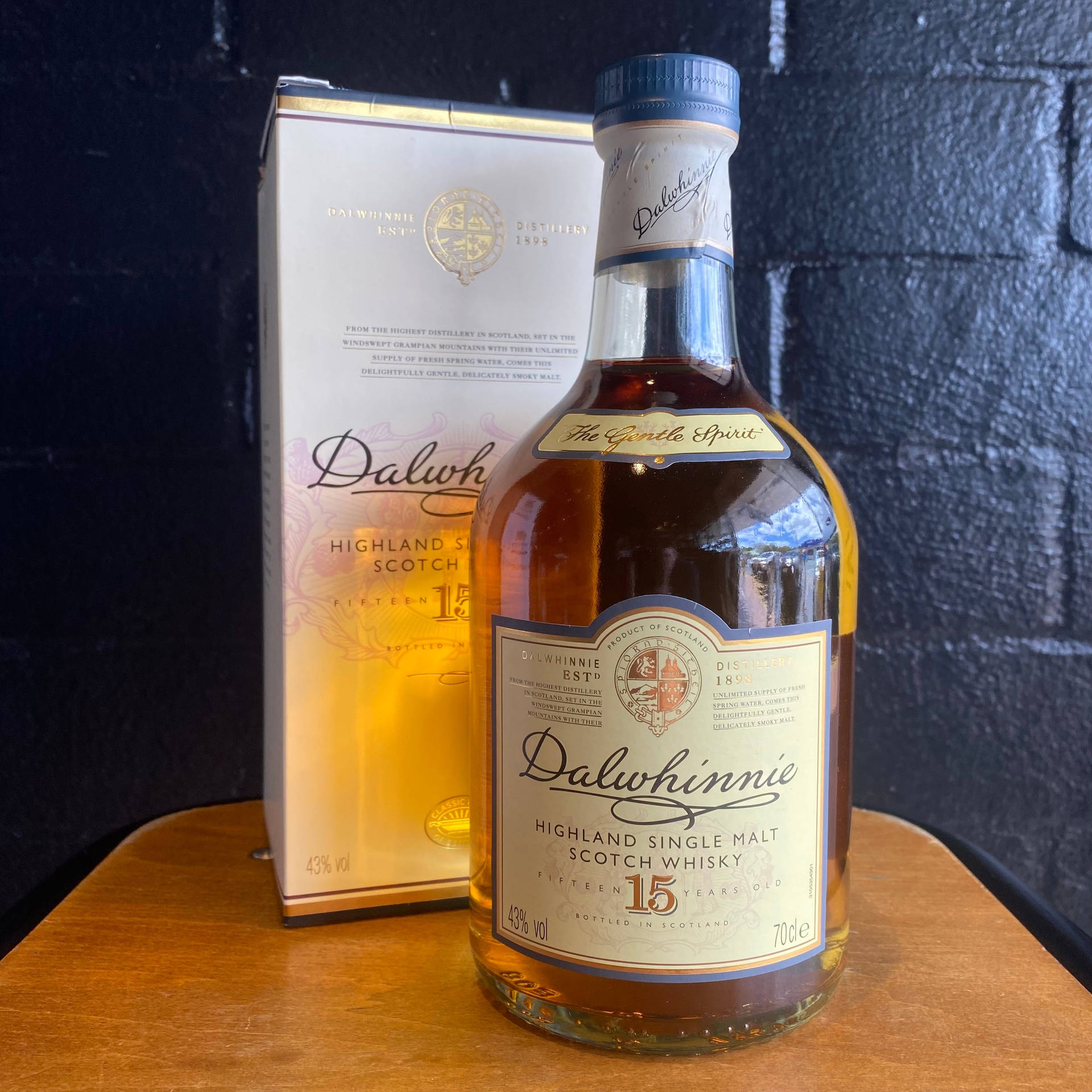 Dalwhinnie 15年威士忌瓶和盒子在木桌上，背景是磚牆。