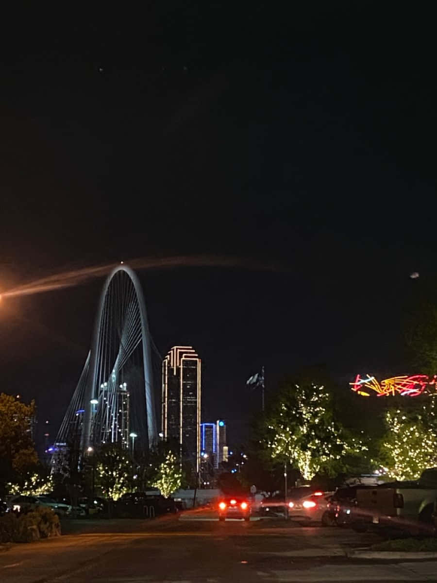 達拉斯縣日落天際線 壁紙 — 夜晚城市景觀，有一座發光的拱橋和燈火通明的摩天大樓，樹木和汽車上裝飾著節日燈飾。