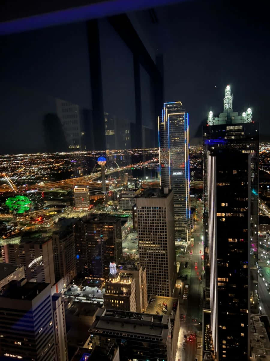 達拉斯縣背景窗景 壁紙 — 迷人的夜景城市景觀，高聳的摩天大樓閃爍著霓虹燈光，下方是廣闊的城市網格。
