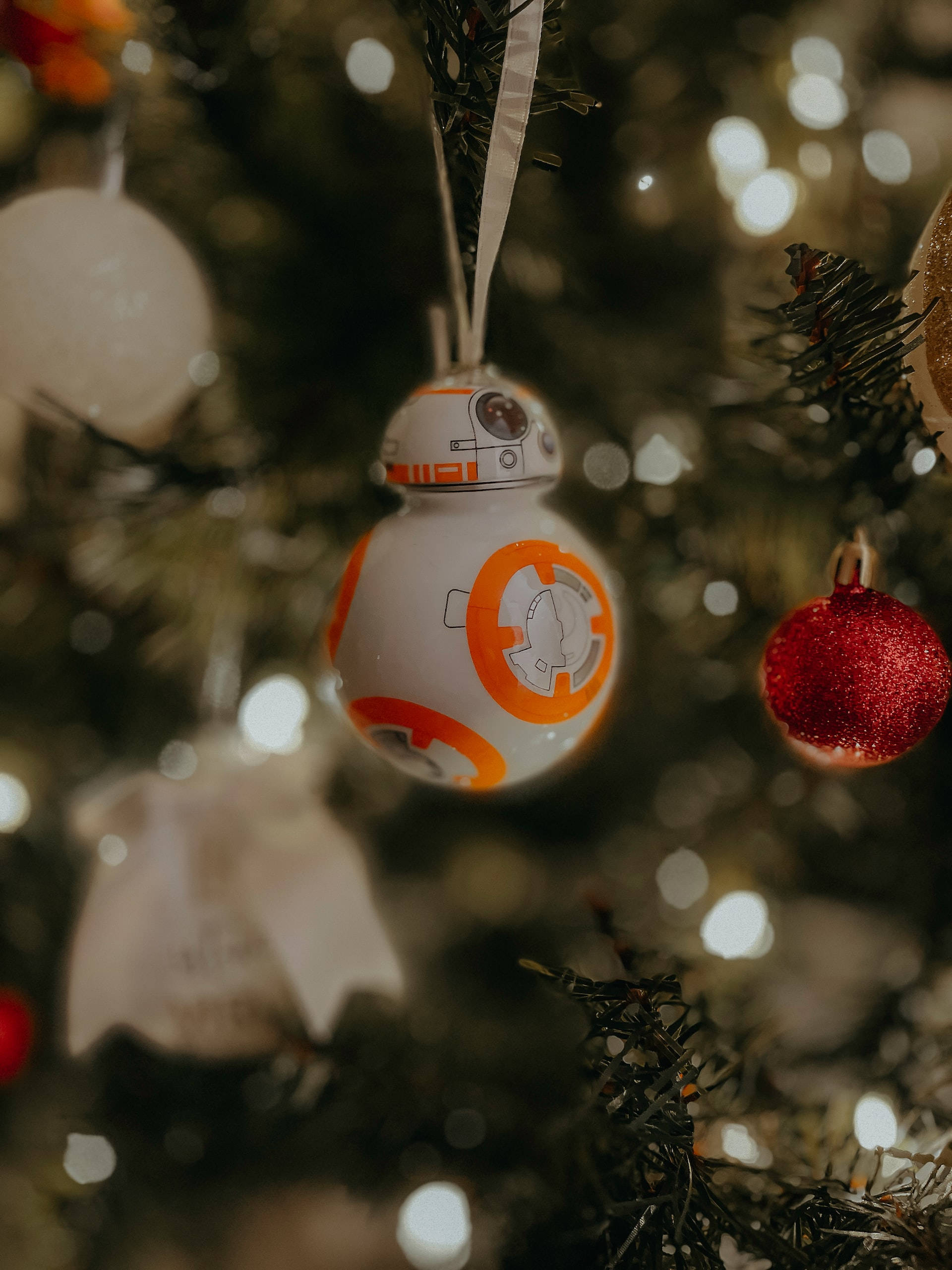 達斯維達與路克天行者在iPhone螢幕上的經典對決 壁紙 — 一個 BB-8 星球大戰裝飾品掛在柔和燈光的聖誕樹上，配有散景燈光和其他節日飾物。