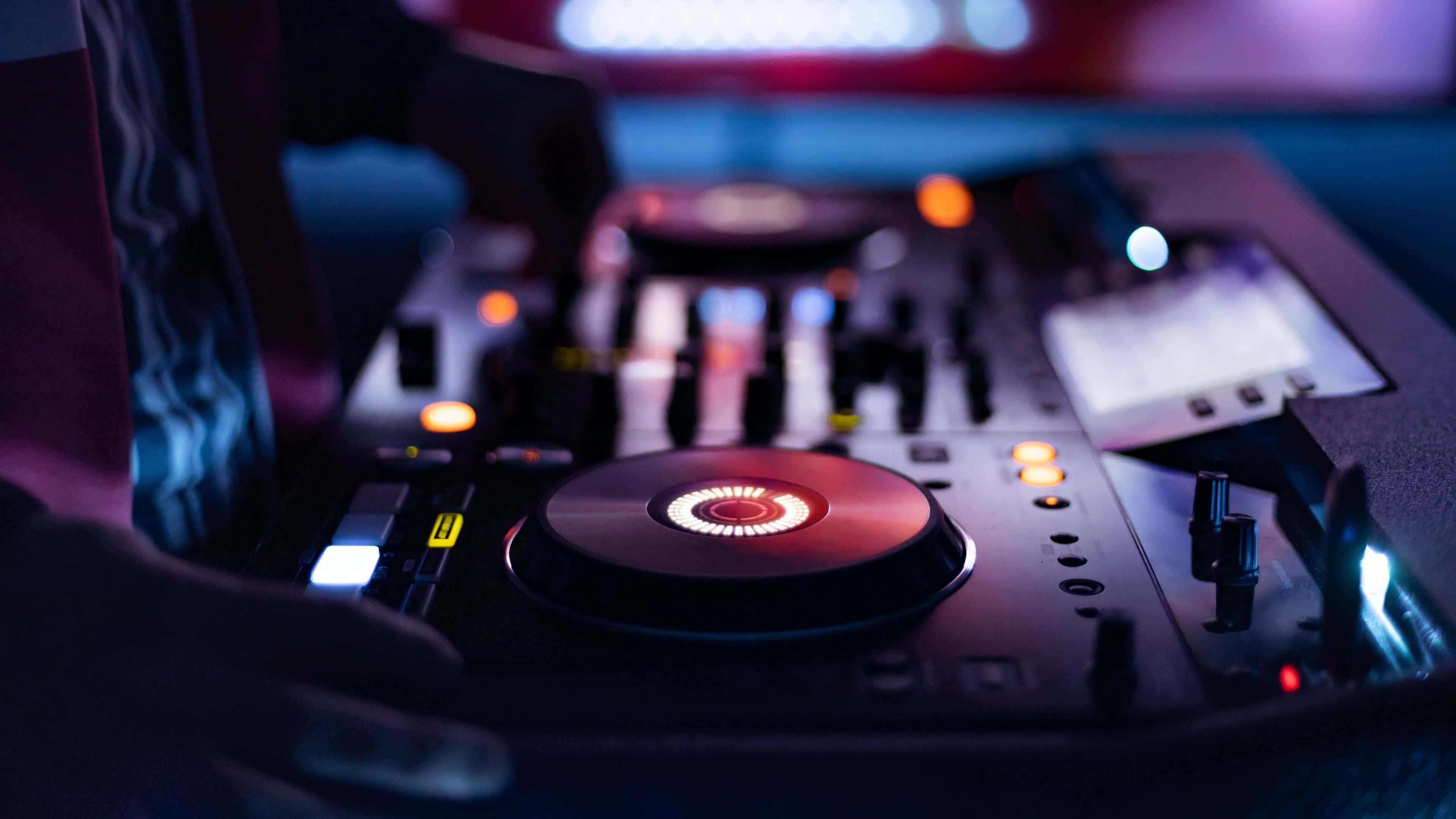 遙控 DJ 音頻混音台 壁紙 — DJ混音器在昏暗的夜總會環境中發出霓虹燈光的特寫。
