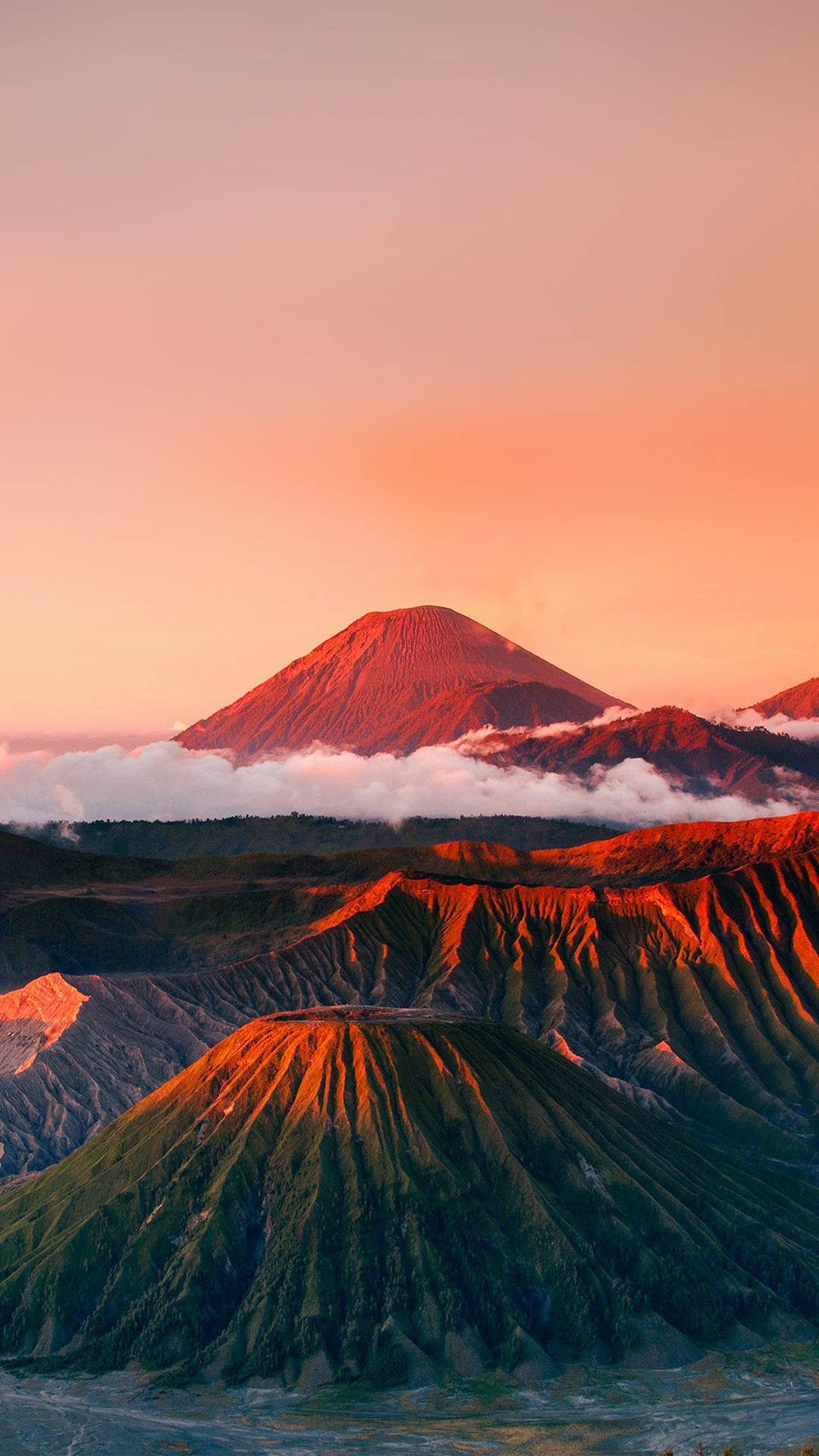 日出時的火山山脈，下方的雲朵在橙色和粉紅色的光芒中閃耀。