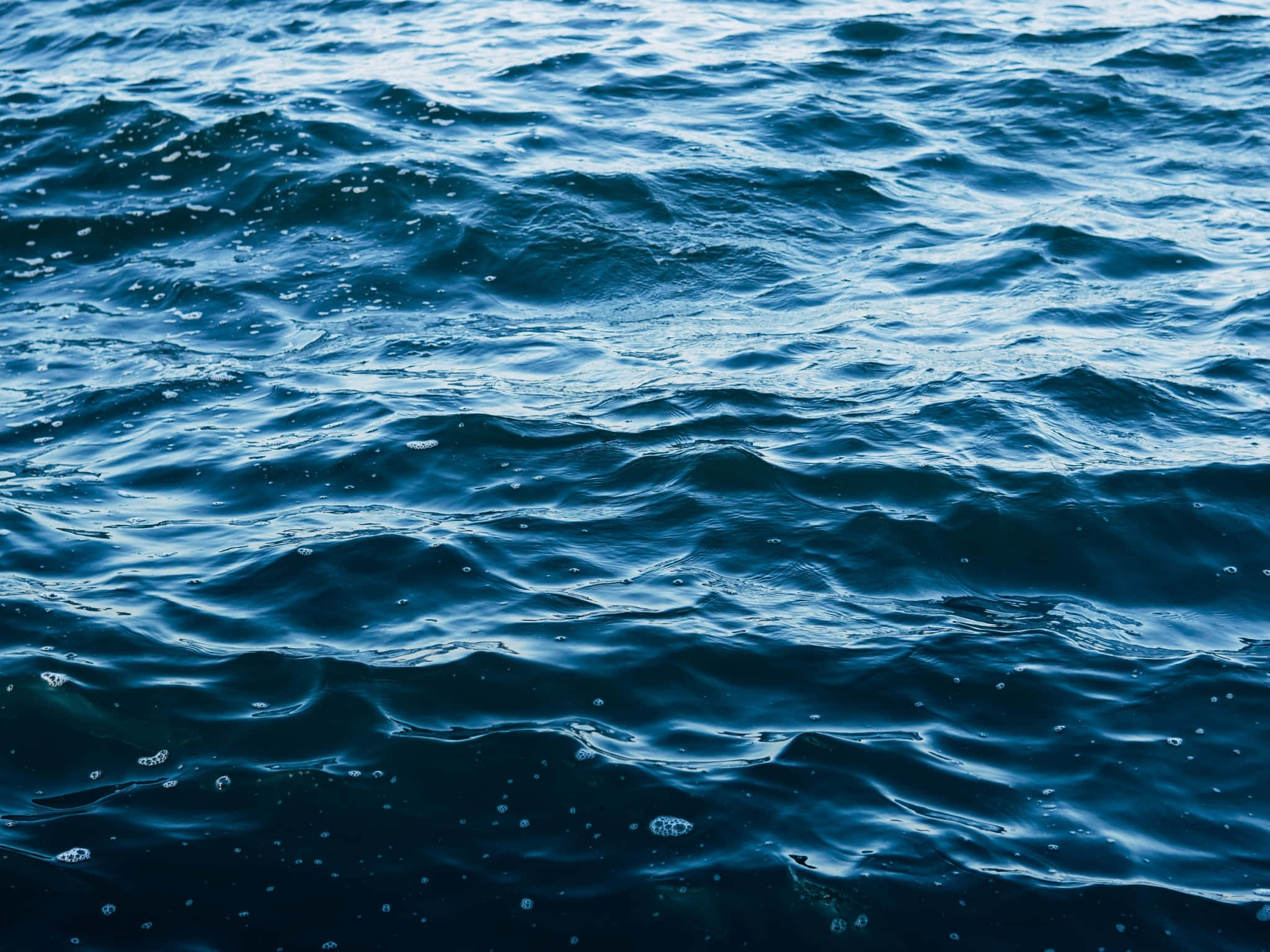 遠眺無盡海洋 壁紙 — 深藍色海洋波浪在柔和日光下泛起帶有紋理的泡沫漣漪。