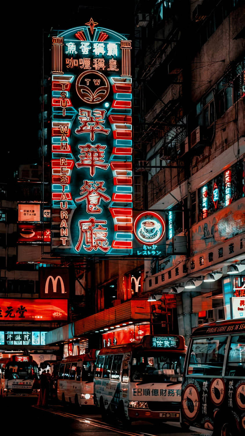 適合 iPhone 屏幕的都市夜景燈光 壁紙 — 充滿活力的霓虹燈照亮了香港繁忙的街道，夜晚有色彩繽紛的巴士和高聳的建築物。