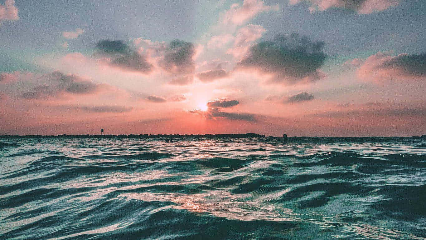 適合休閒出遊的時尚學院風造型 壁紙 — 夕陽在雲層後發光，在紋理化的海面上將天空染成粉紅色和橙色。