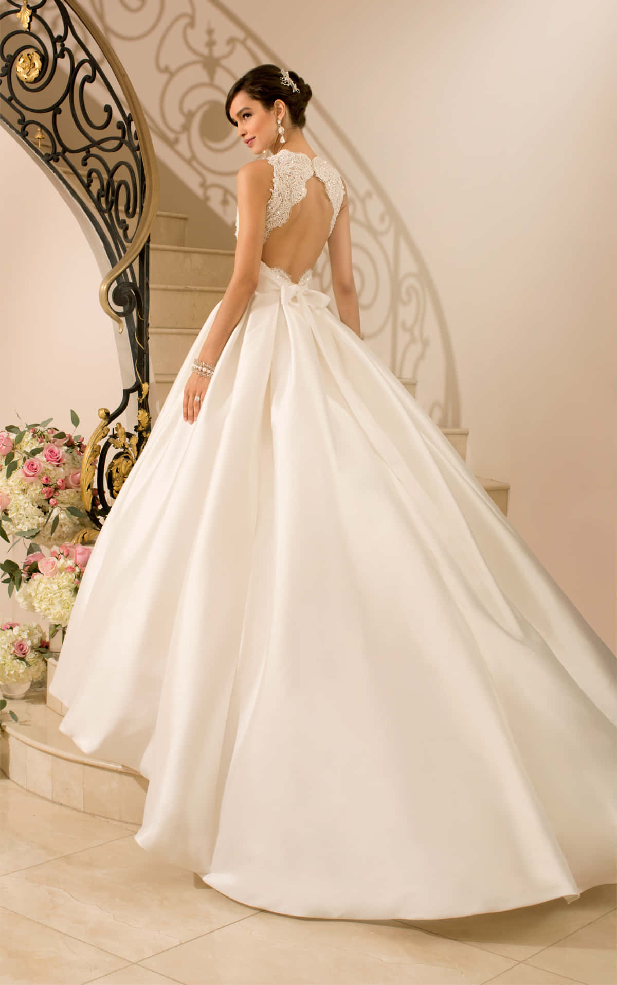 適合公主的絕美婚紗 壁紙 — 一位身穿白色舞會禮服、背部有蕾絲設計的新娘，優雅地站在大理石樓梯上，旁邊是花卉佈置。
