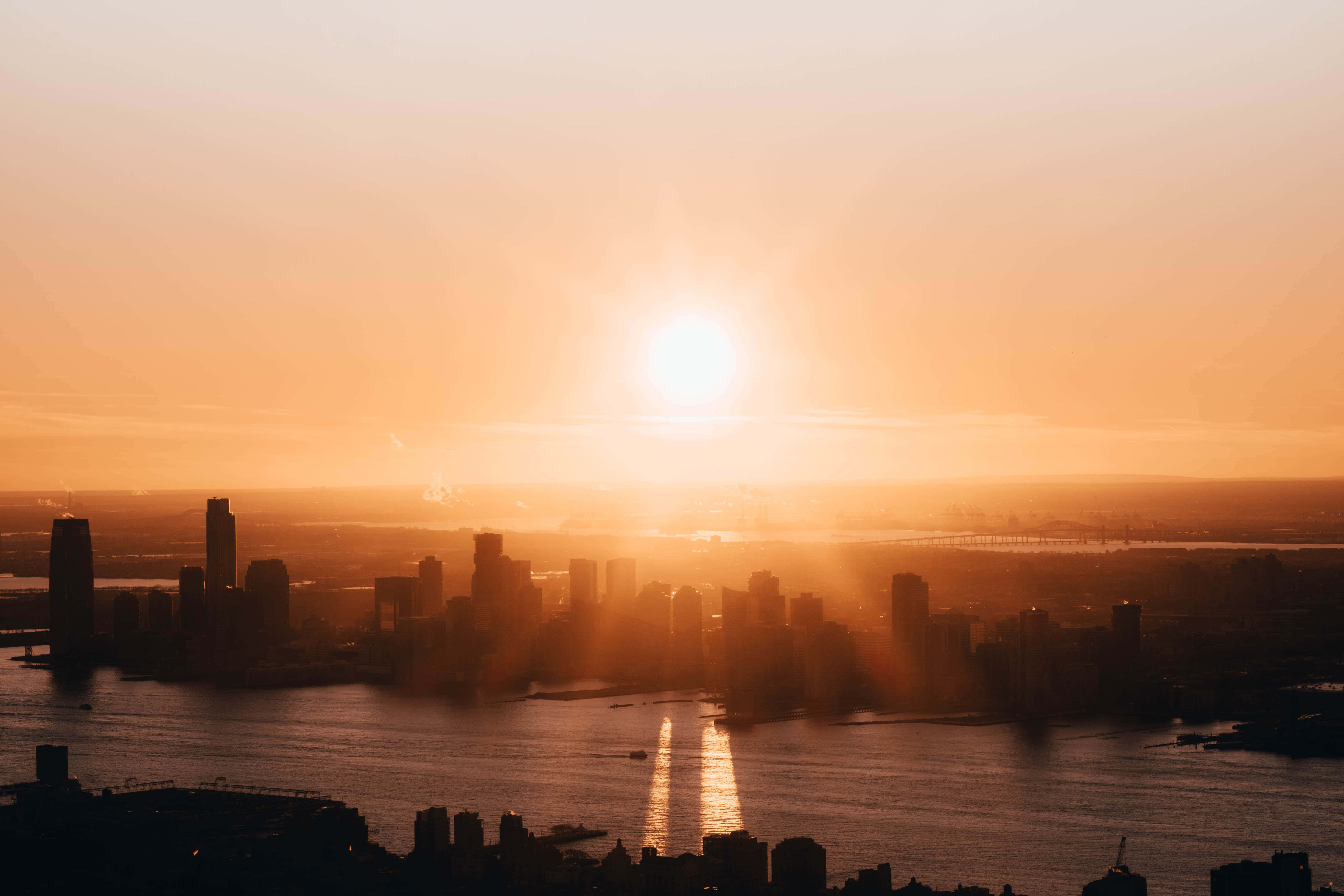 適合為任何項目增添獨特觸感的淺藍抽象背景 壁紙 — 夕陽將廣闊的城市天際線沐浴在金色光芒中，光線穿透薄霧，映照在反射的水道上。