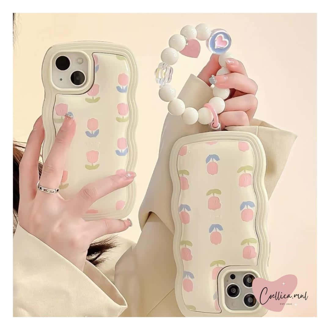 適用於 iPhone 的寧靜抽象美學壁紙 壁紙 — 一個人喺柔和米色背景前，手持兩個奶油色、帶有粉彩鬱金香圖案嘅手機殼同一個相配嘅珠仔手帶。