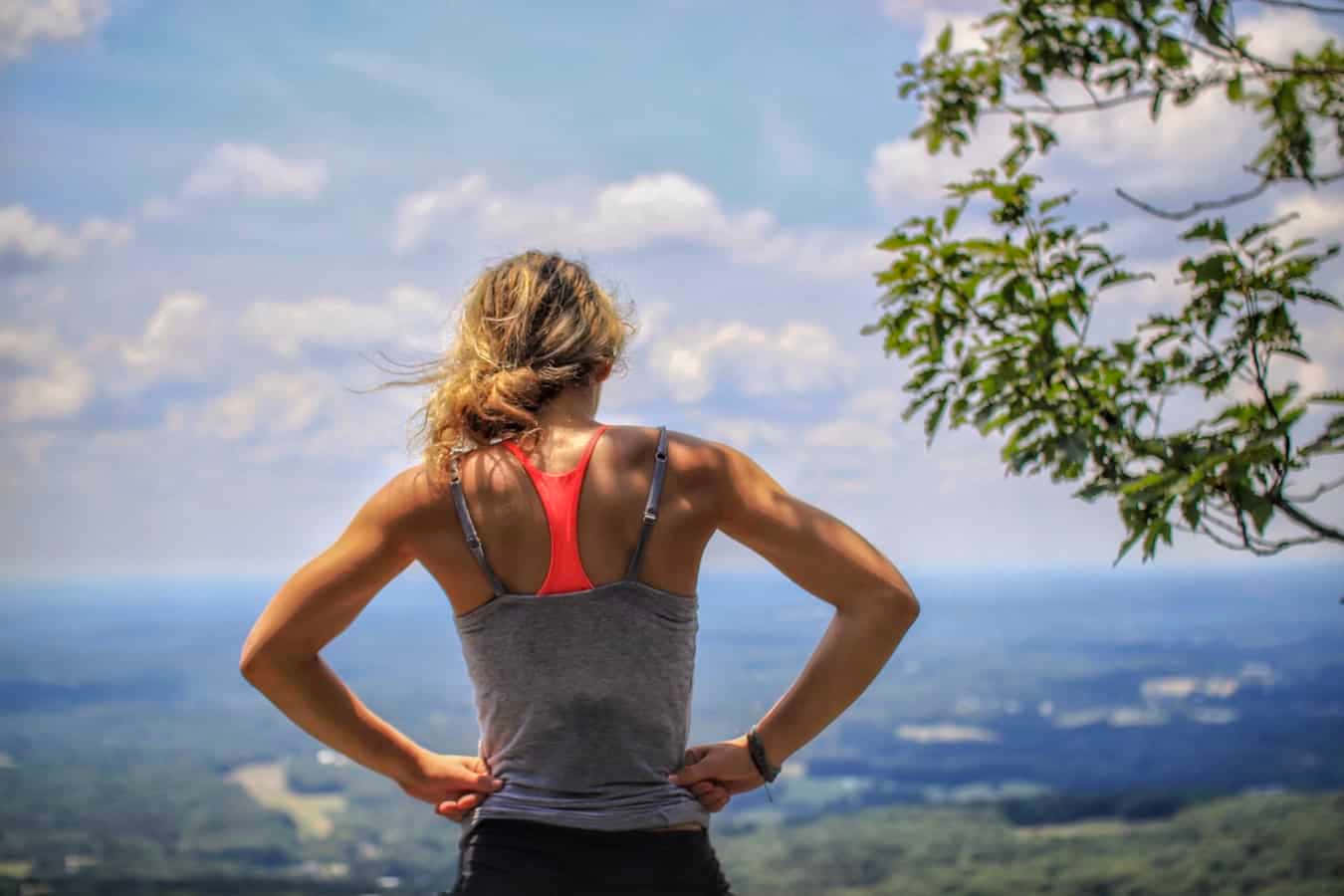 一位穿著運動服的女士站在山頂上，俯瞰著風景如畫的山谷。