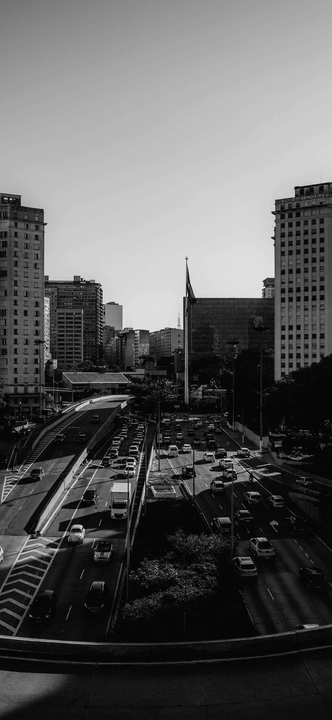 選擇完美的黑白 iPhone 壁紙 — 一張高角度黑白照片，拍攝繁忙的城市高速公路，兩旁高樓林立，天空晴朗。