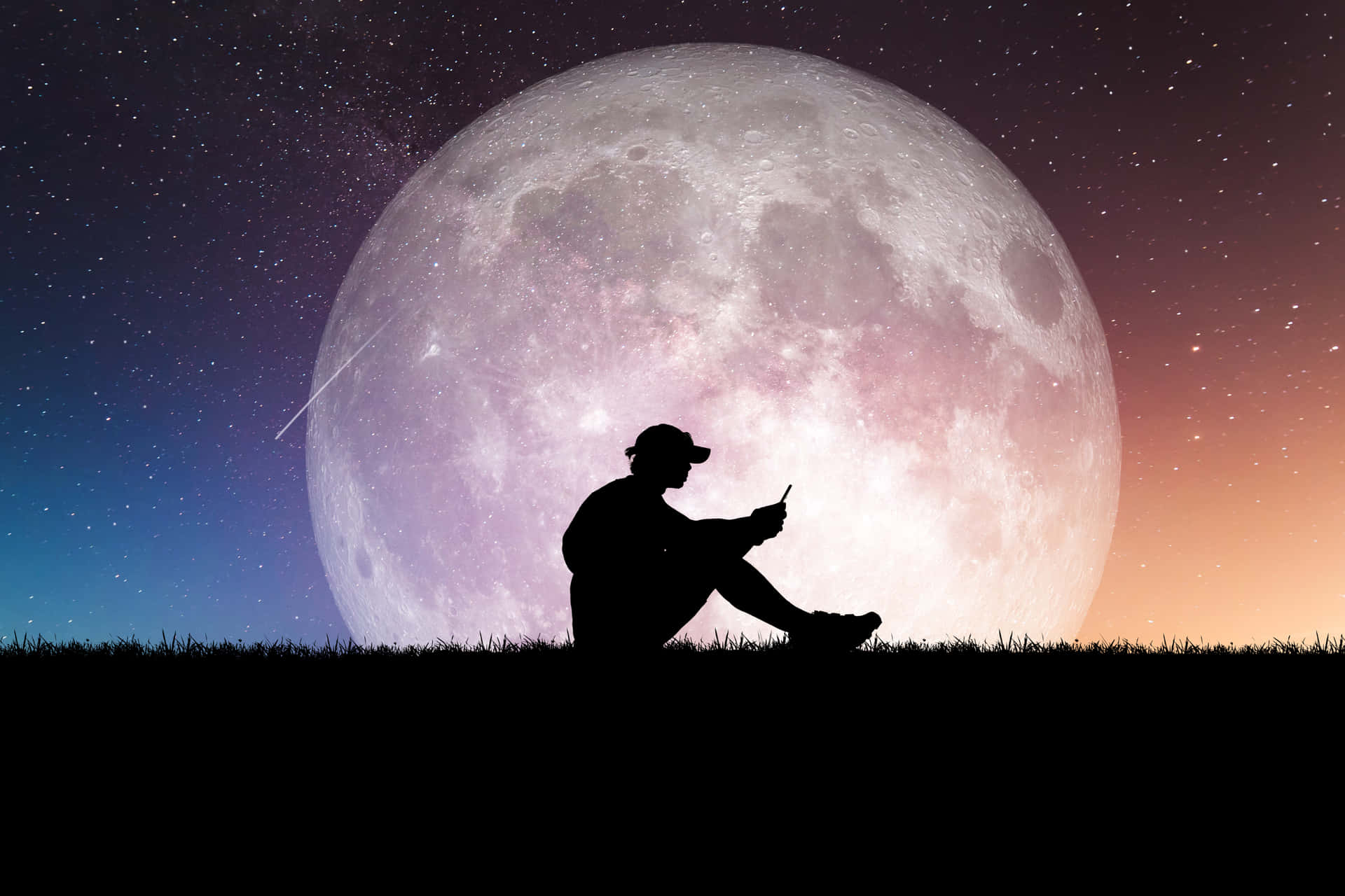 人在草地上看手機，背景是巨大的月亮和星星