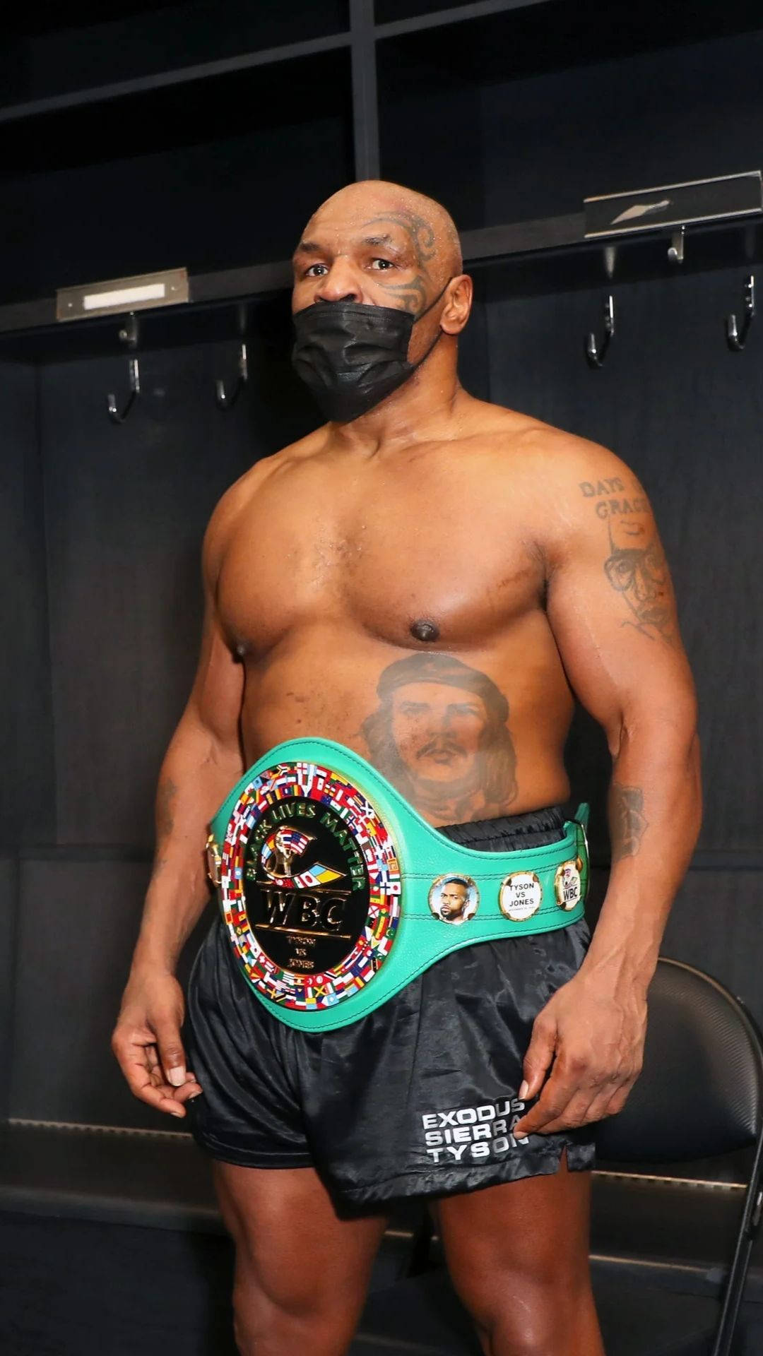 邁克·泰森 戴面罩 壁紙 — Mike Tyson 站在更衣室，戴著黑色口罩和綠色冠軍腰帶。