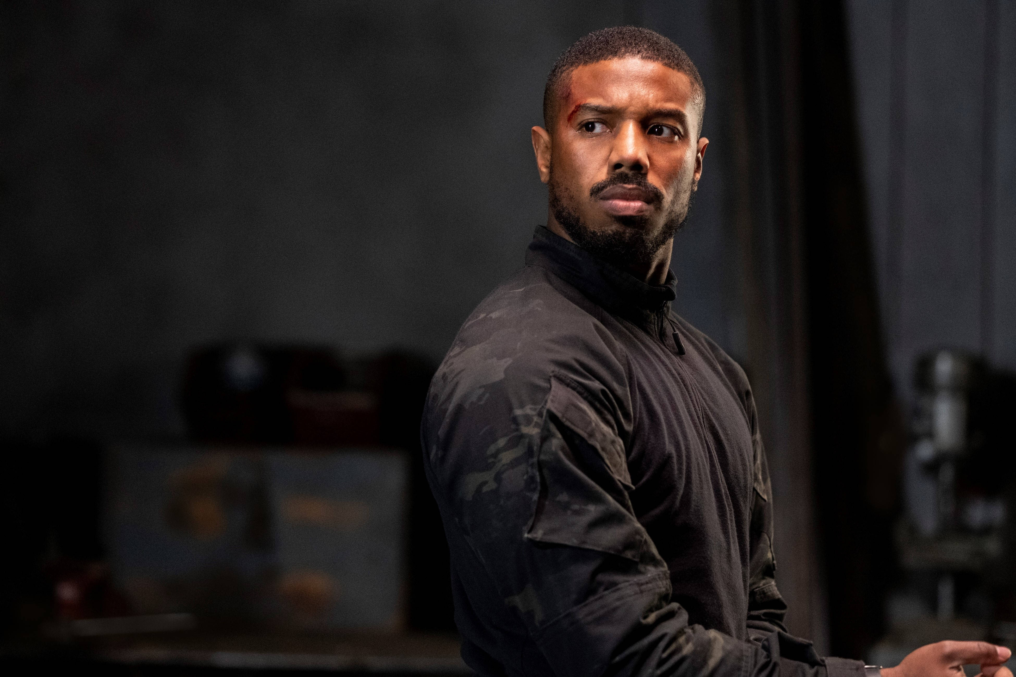 邁克爾·B·喬丹《無間》 壁紙 — 一個額頭流血的男人在昏暗的工業環境中專注地凝視。